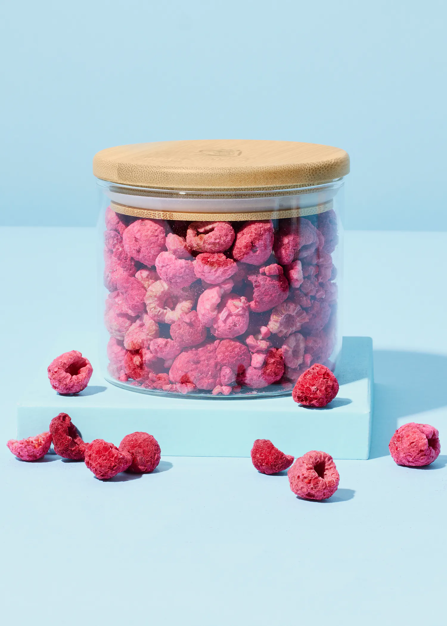 a glass jar with a wooden lid filled with raspberries