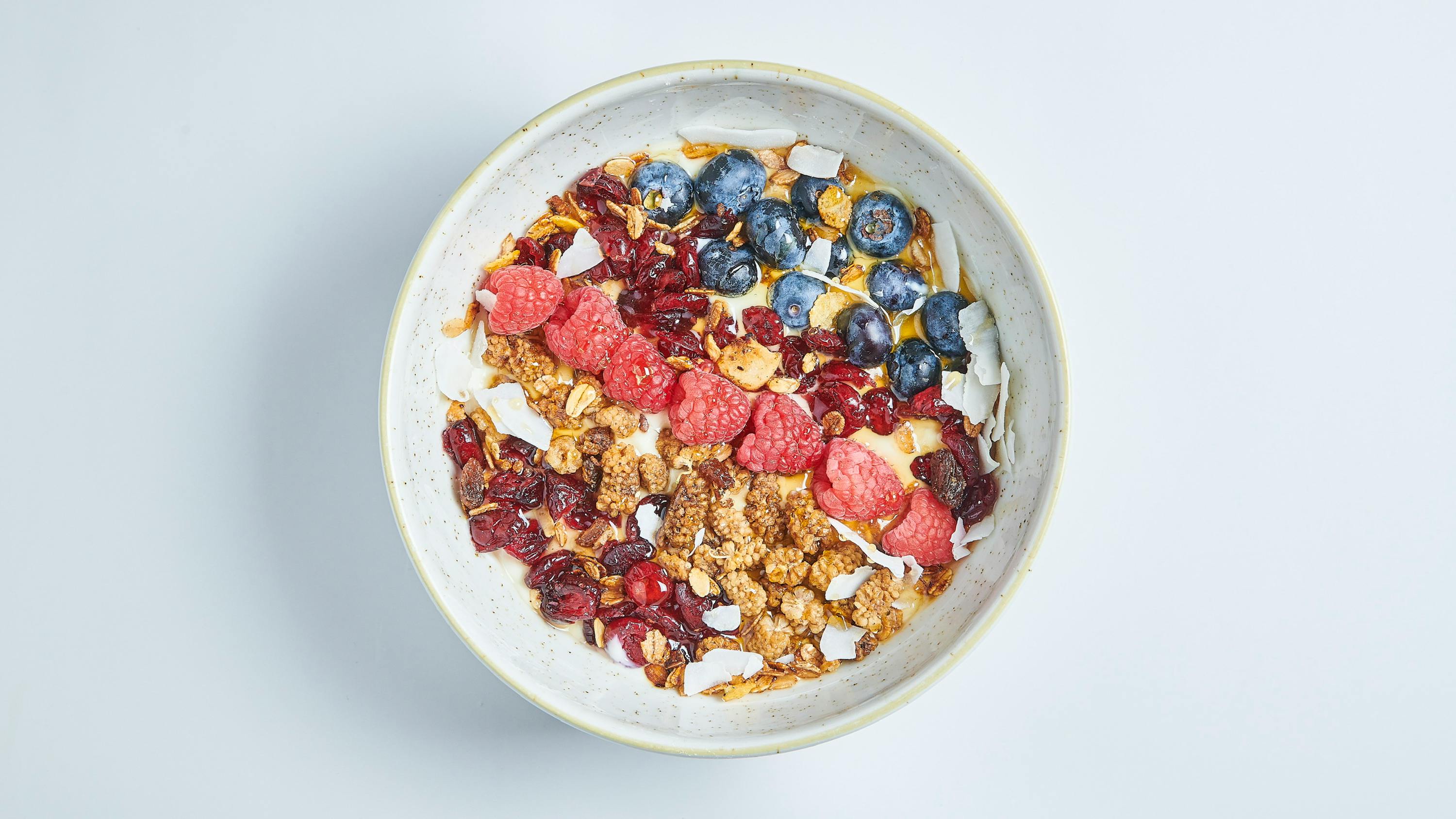 a bowl of granola with blueberries raspberries cranberries and coconut