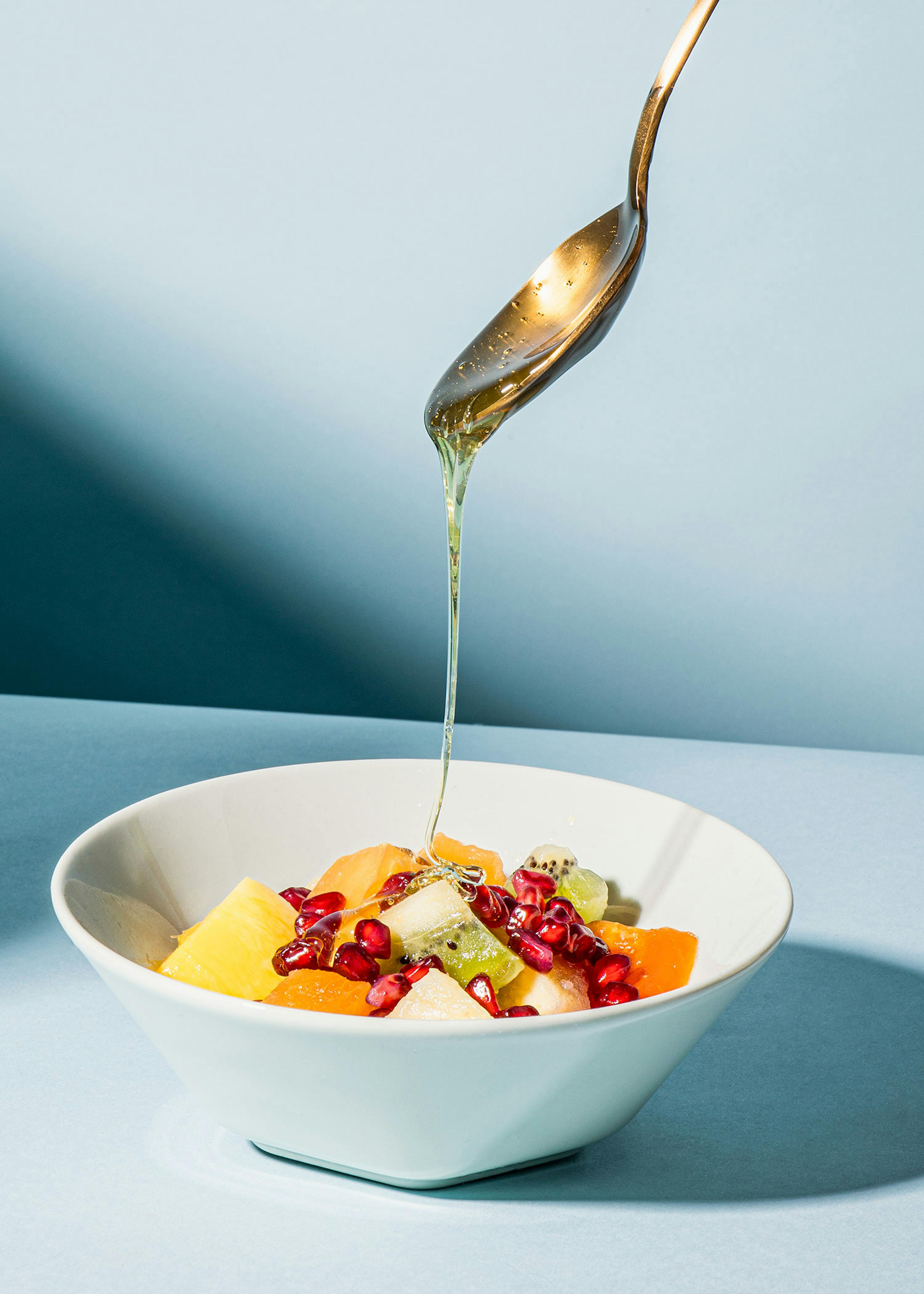 a bowl of fruit is being poured with syrup from a spoon
