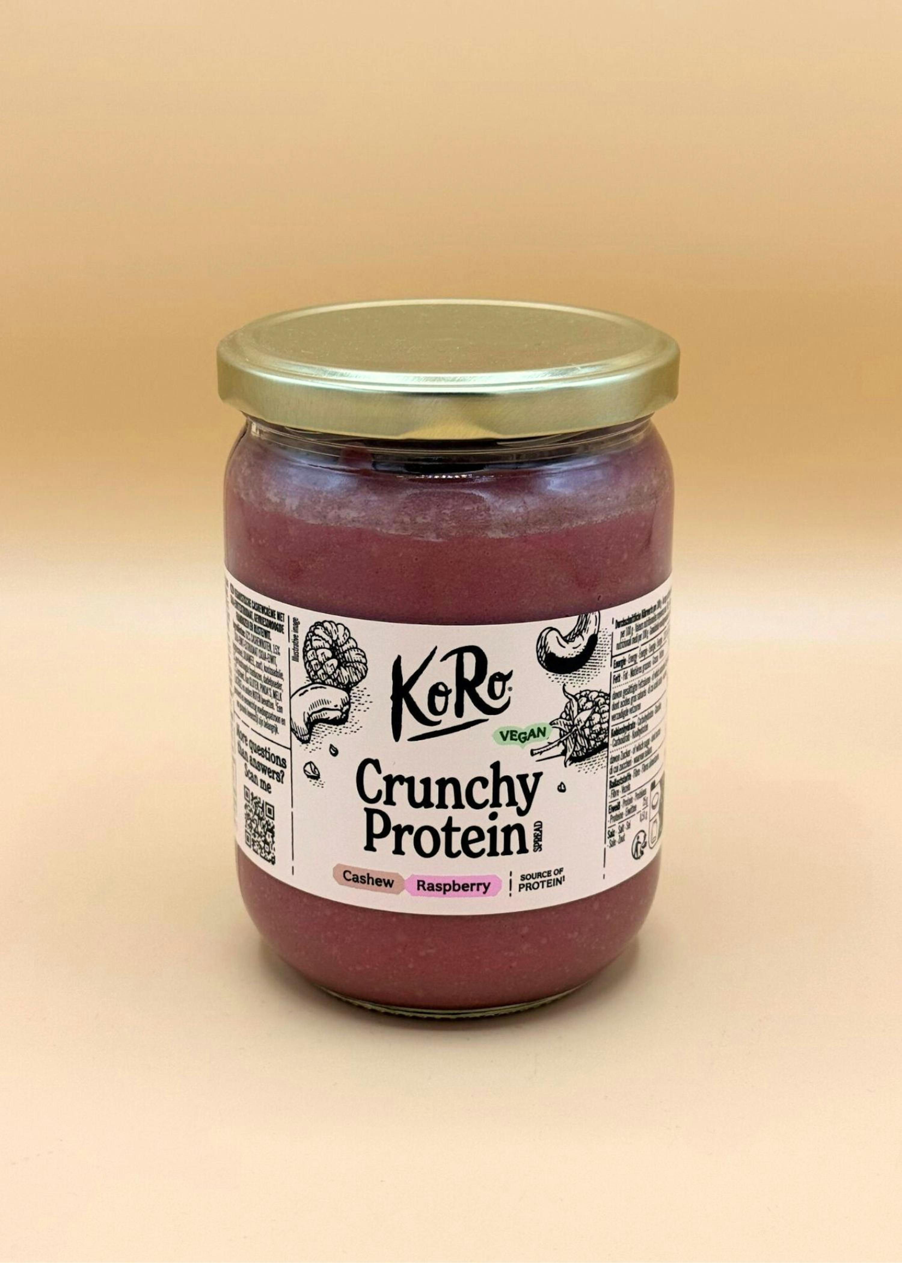 un barattolo di crema spalmabile vegana KoRo crunchy protein al gusto di anacardi e lamponi, con coperchio dorato e il contenuto di colore rosso-violaceo.
