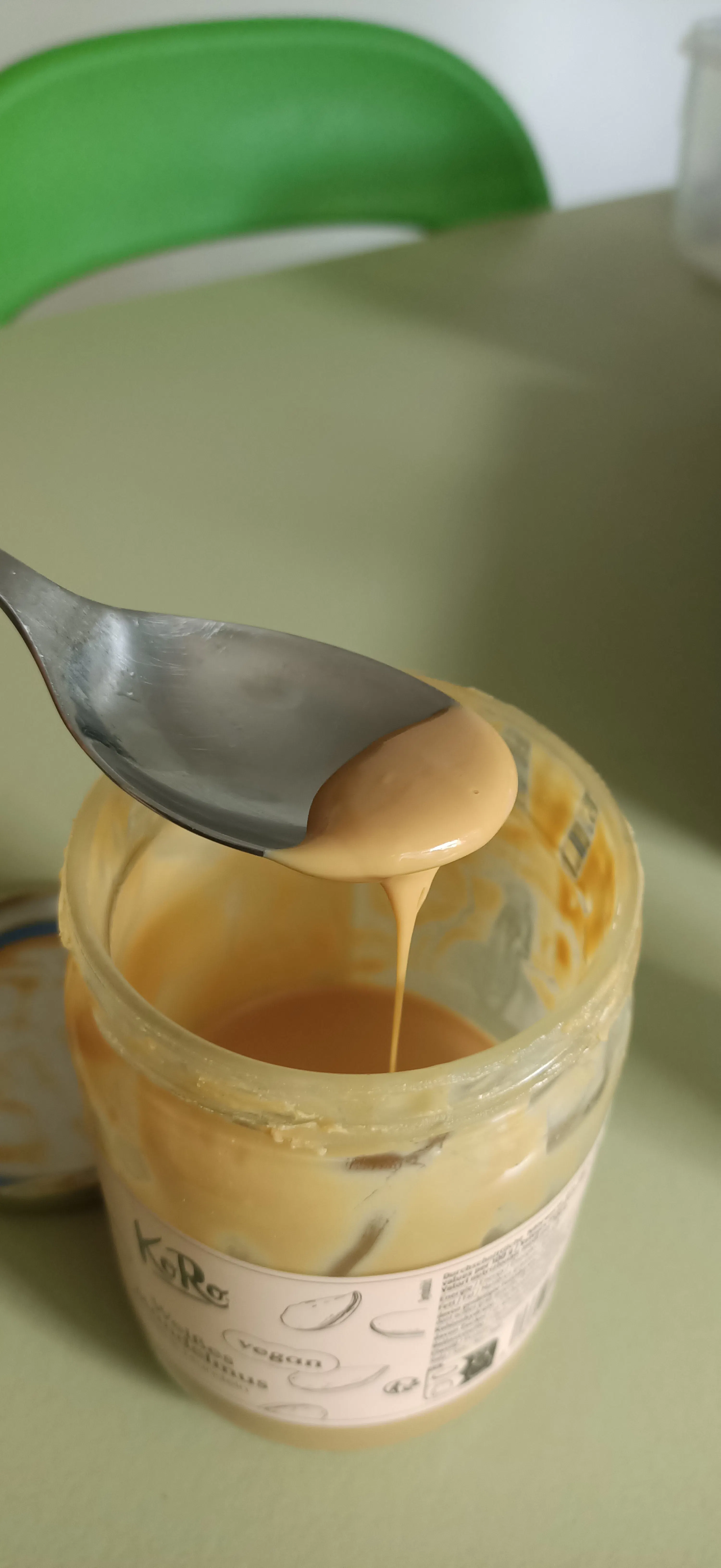 un cucchiaio con una sostanza cremosa color caramello che gocciola in un barattolo di vetro con l'etichetta 'k-ro vegan'.