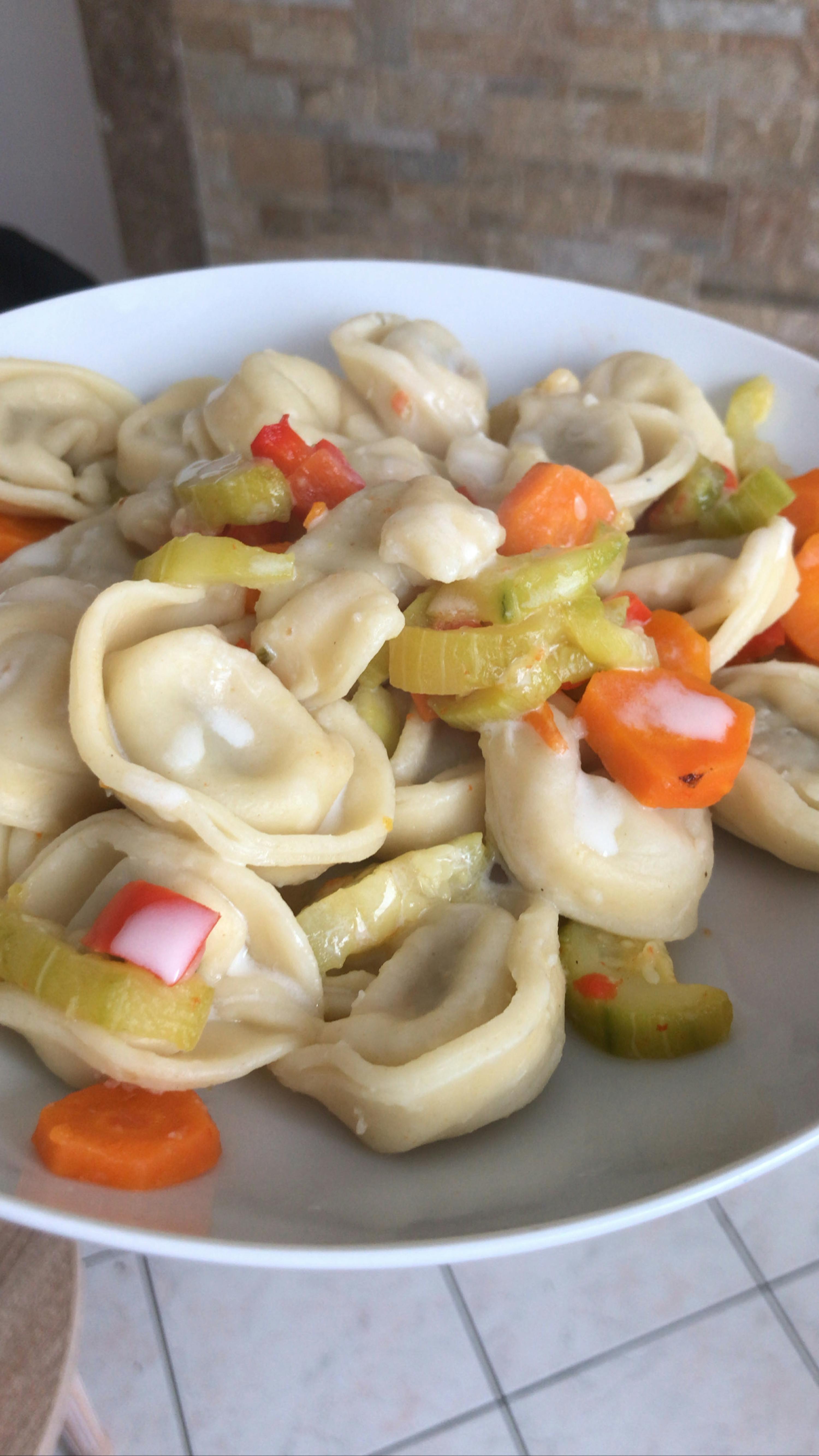a white plate topped with pasta and vegetables on a tiled floor