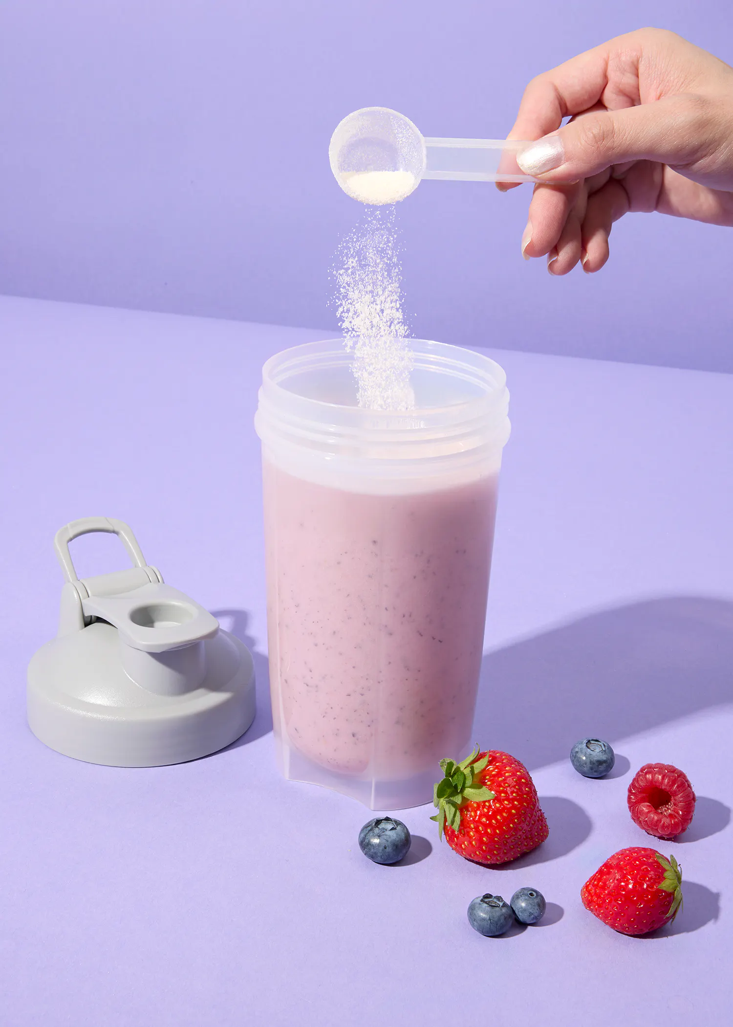 Eine Frau gießt einen Smoothie in einen Shaker mit Erdbeeren und Blaubeeren darauf