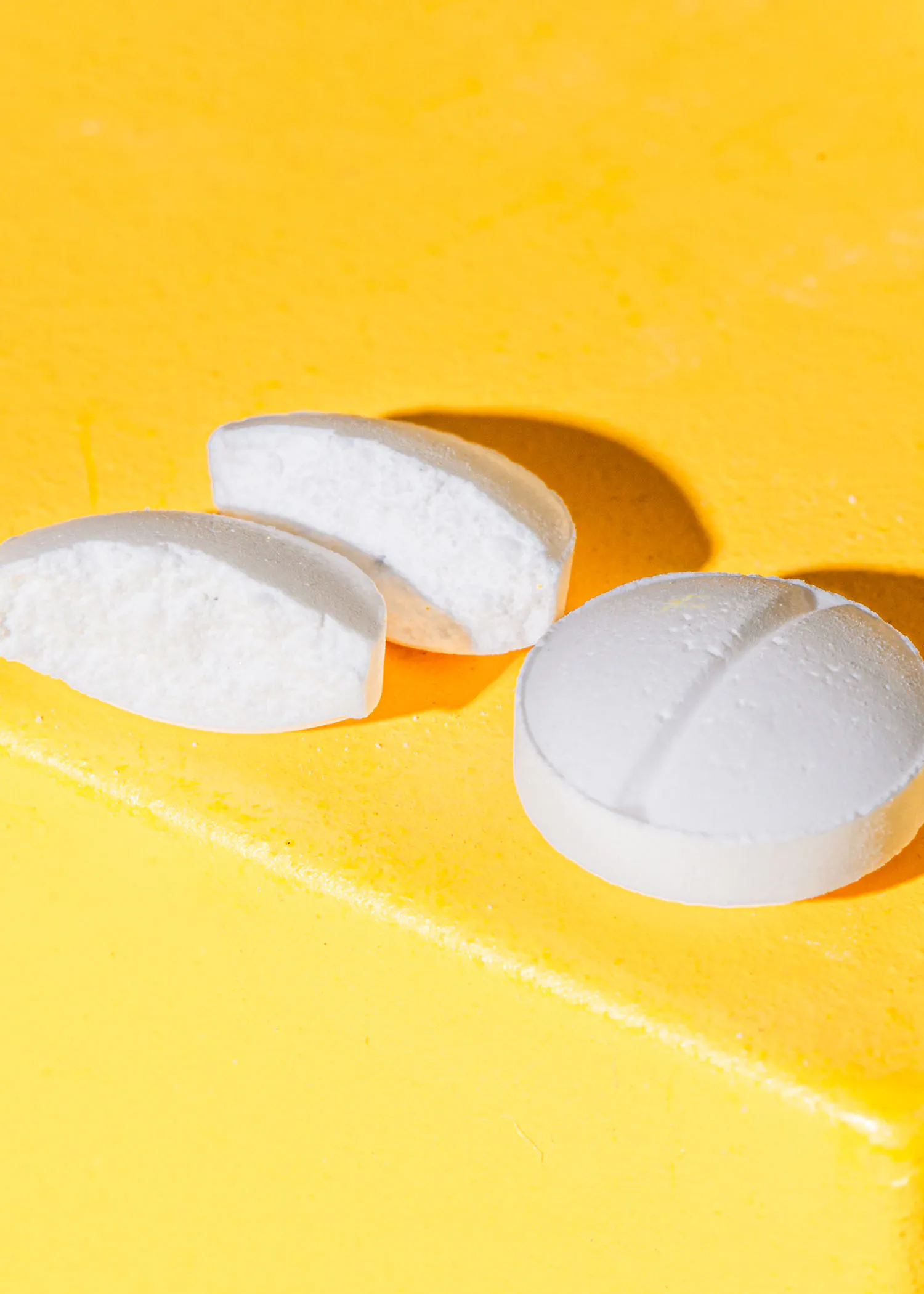 une pilule blanche est coupée en deux sur un fond jaune