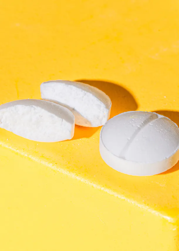 une pilule blanche est coupée en deux sur un fond jaune