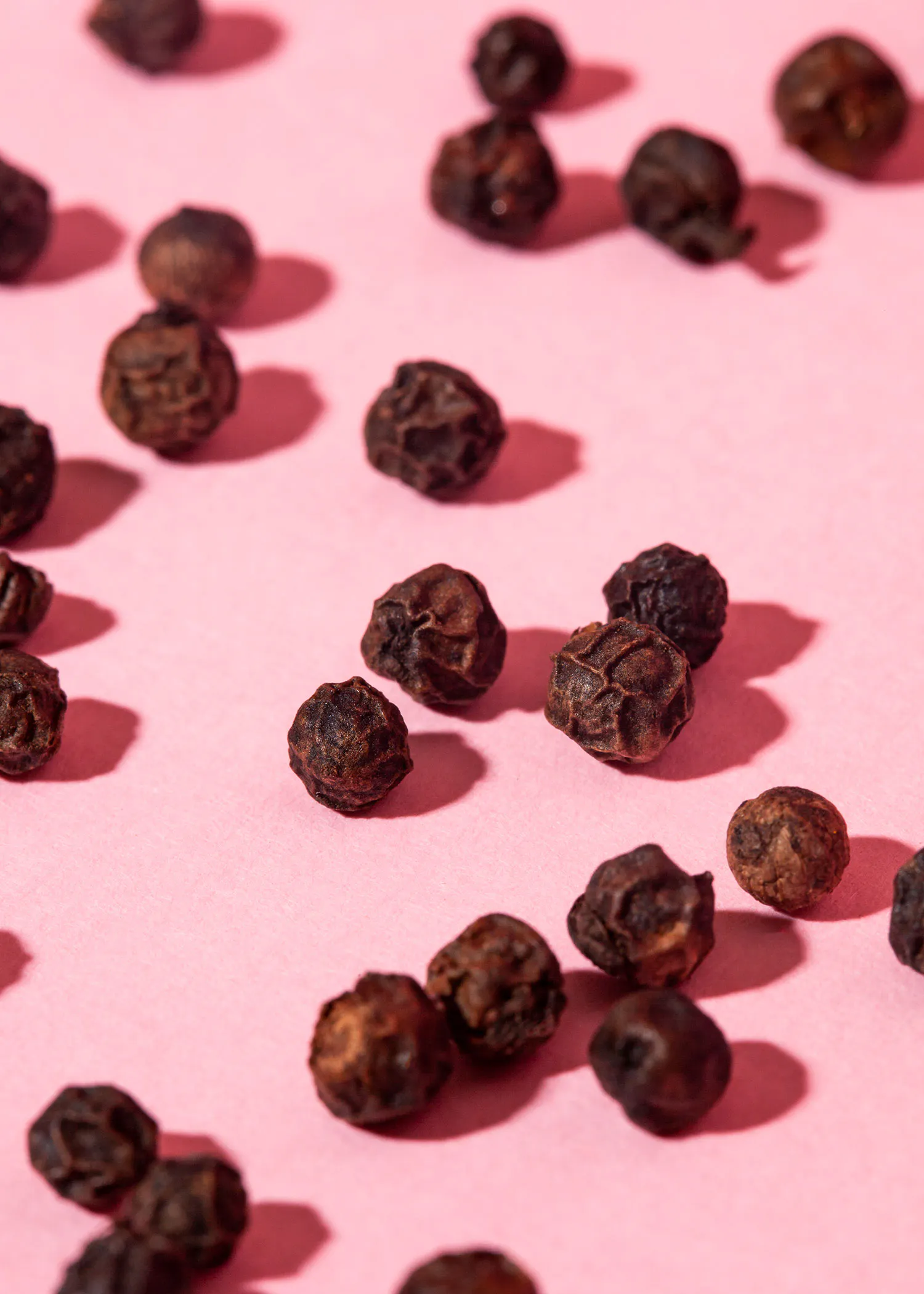 black peppercorns on a pink surface with shadows