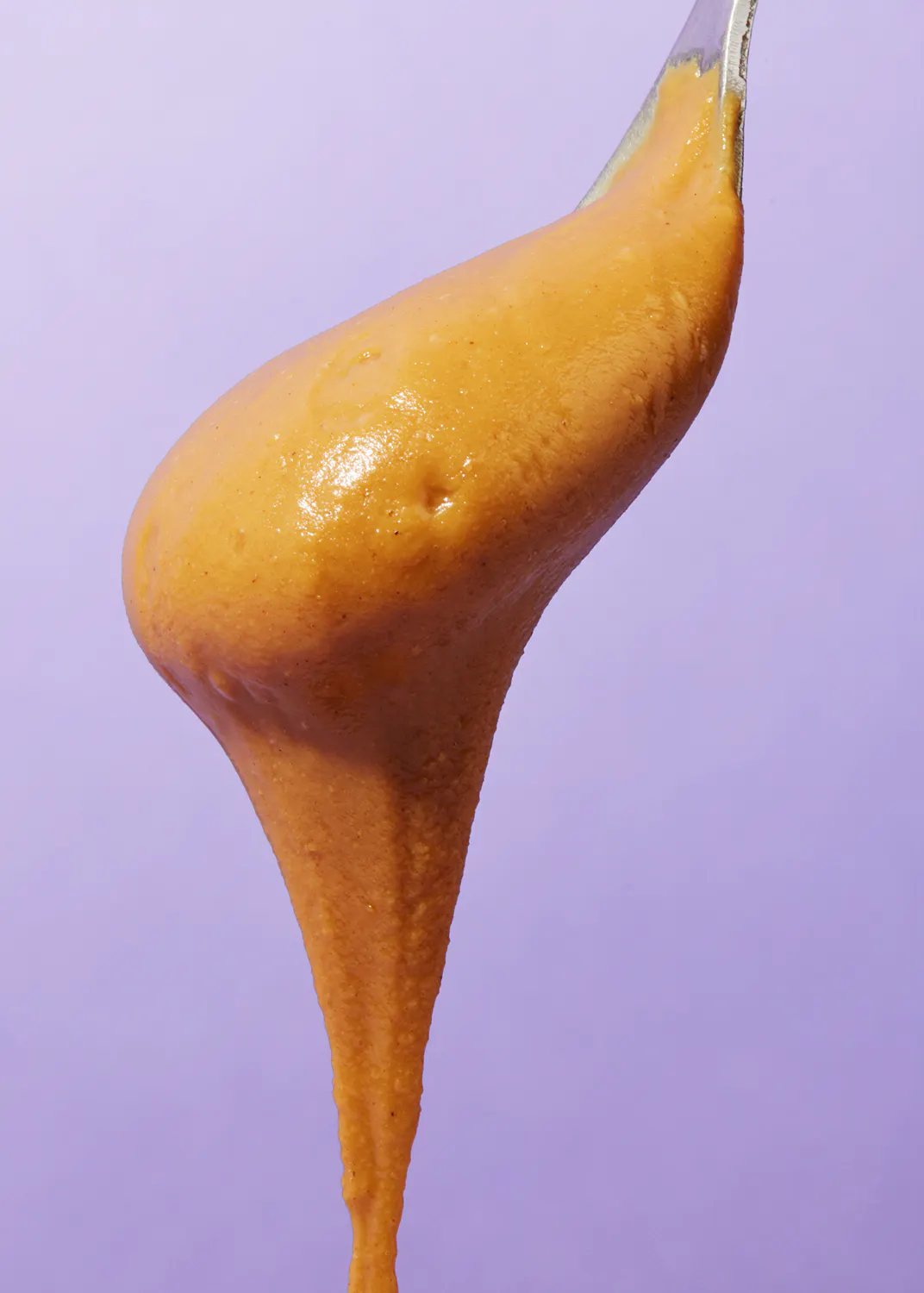 a close up of a spoon filled with orange sauce on a purple background