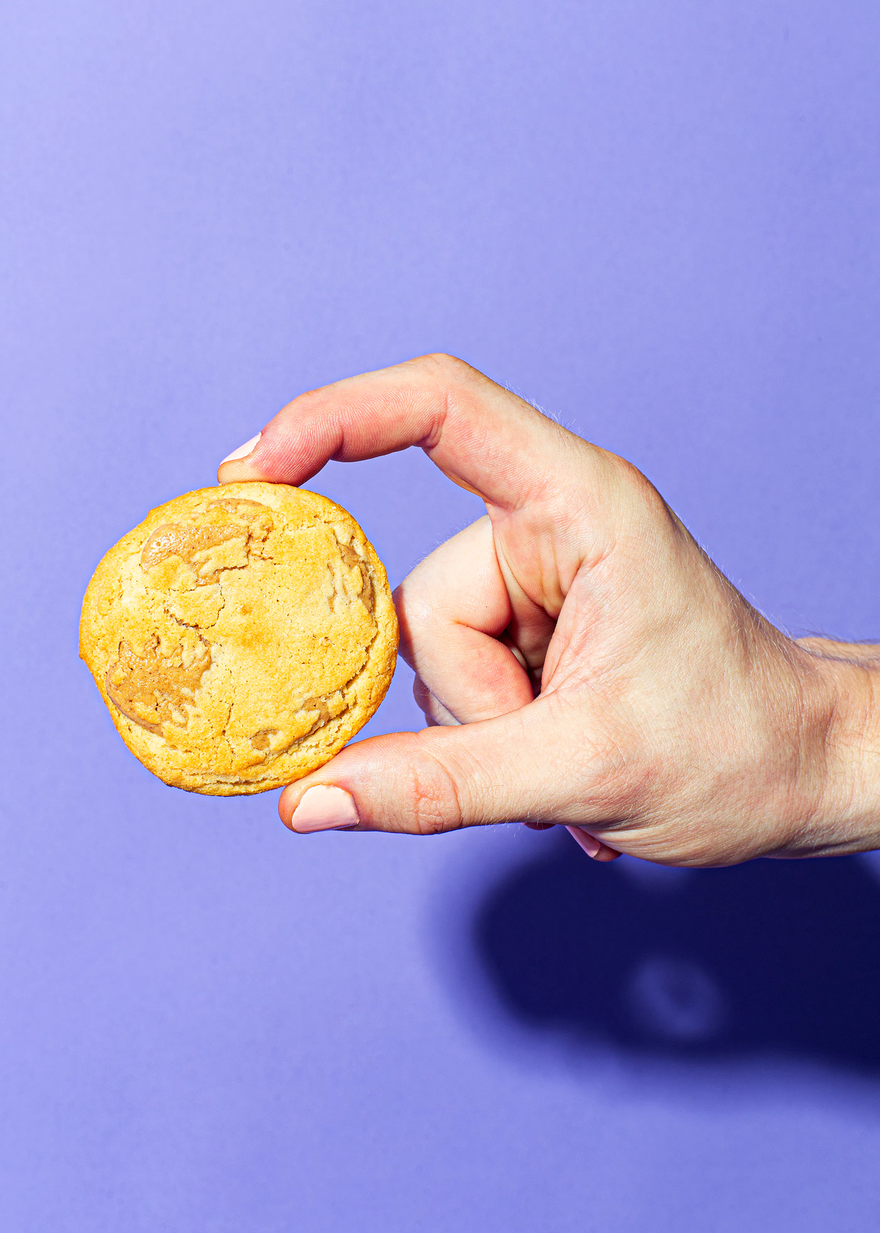 a hand holding a cookie on a purple background