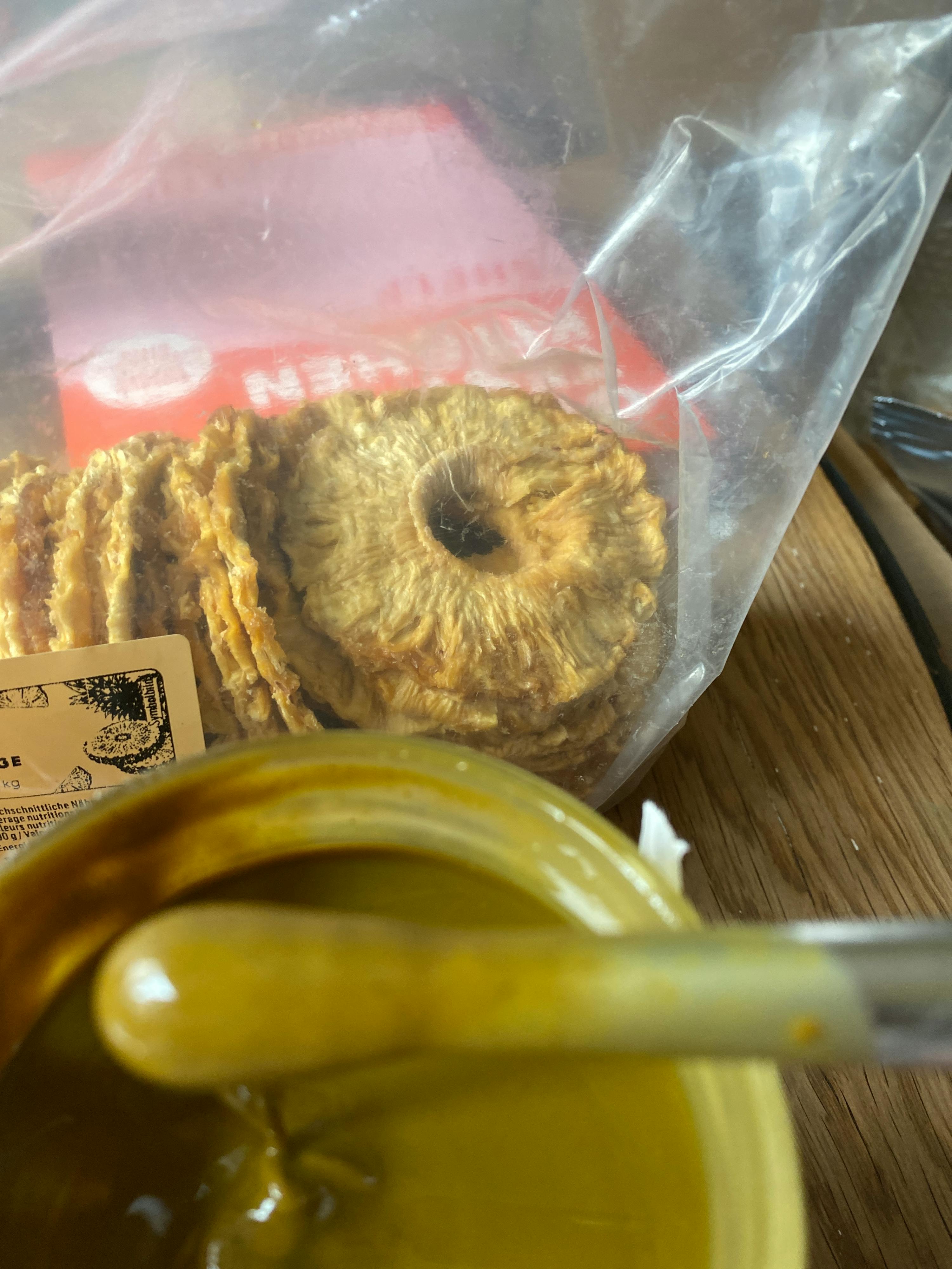a bag of pineapple slices sits on a table next to a jar of honey