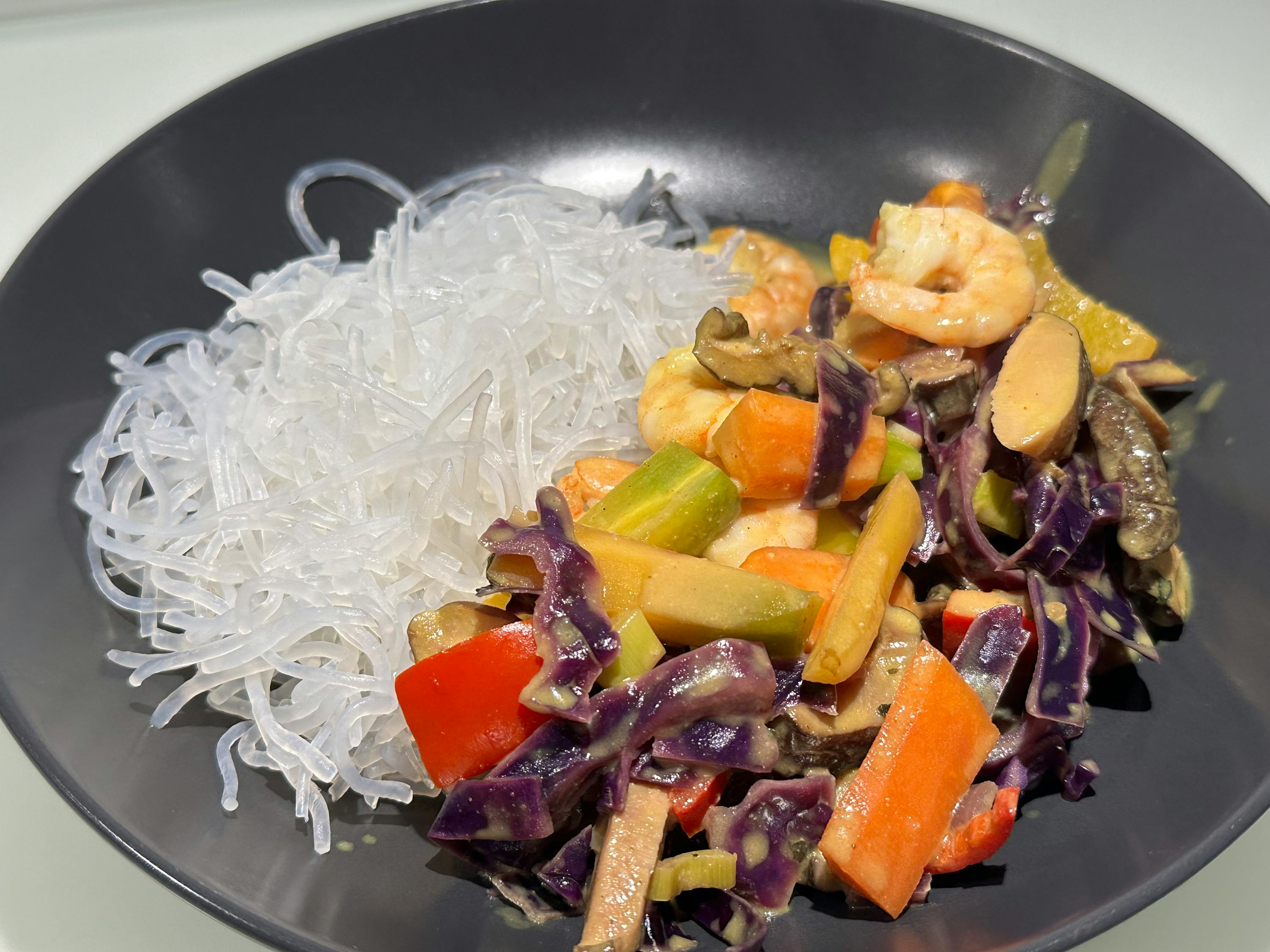 ein teller mit glasnudeln und einem garnelen-gemüse-wok mit rotkohl, karotten und pilzen.