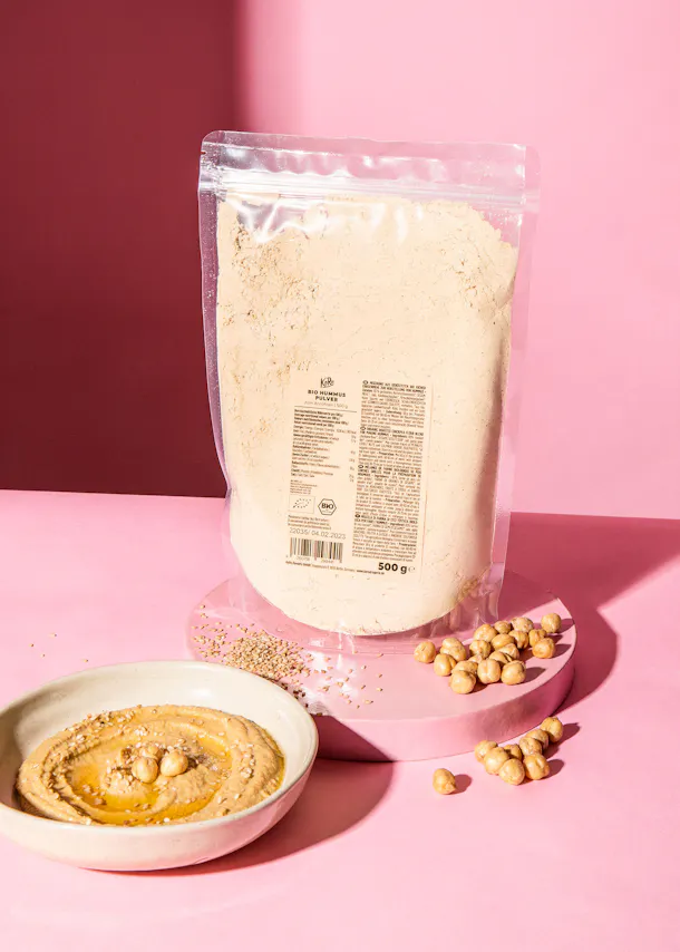 un sac de farine est assis sur une table rose à côté d' un bol de hummus