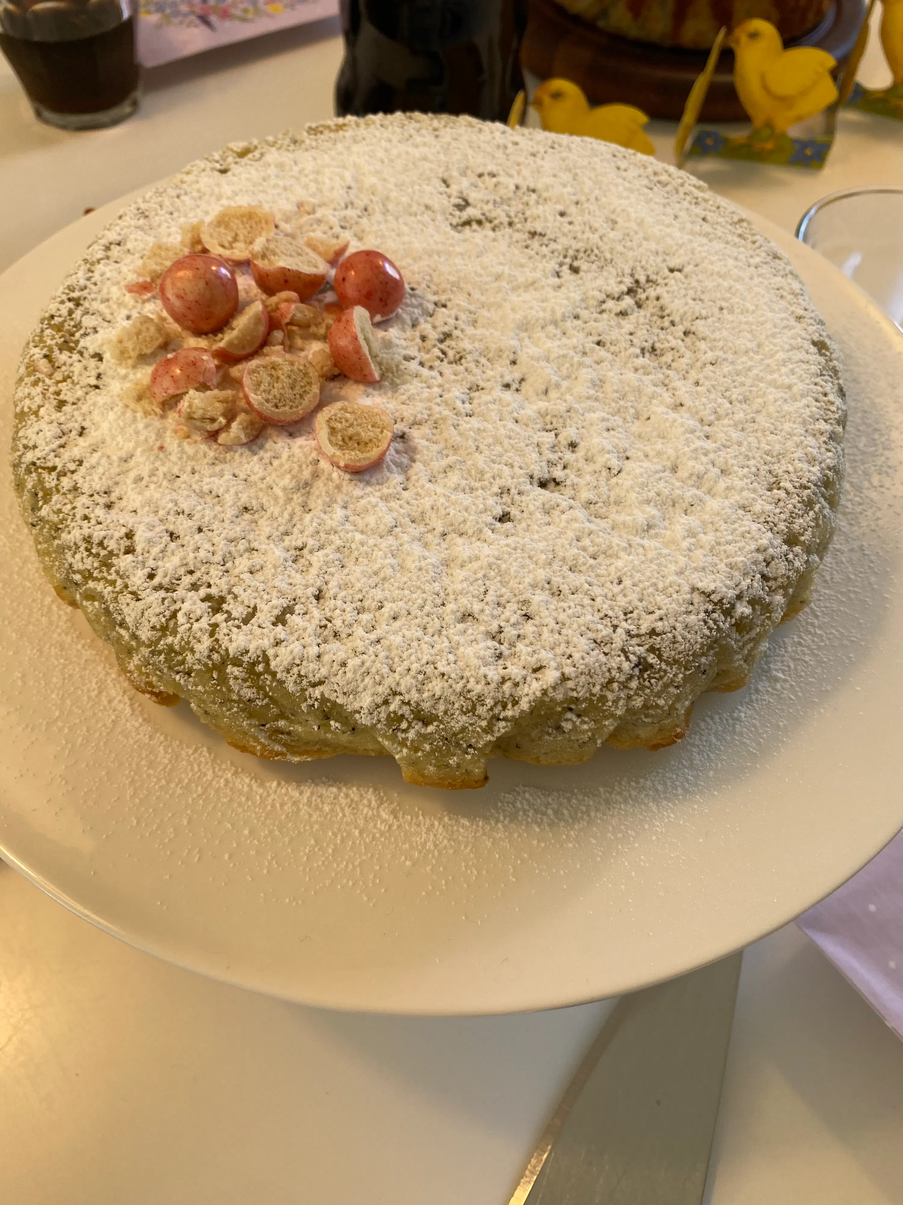 ein runder kuchen, bestäubt mit puderzucker und dekoriert mit roten und beigen süßigkeiten, auf einem weißen teller.