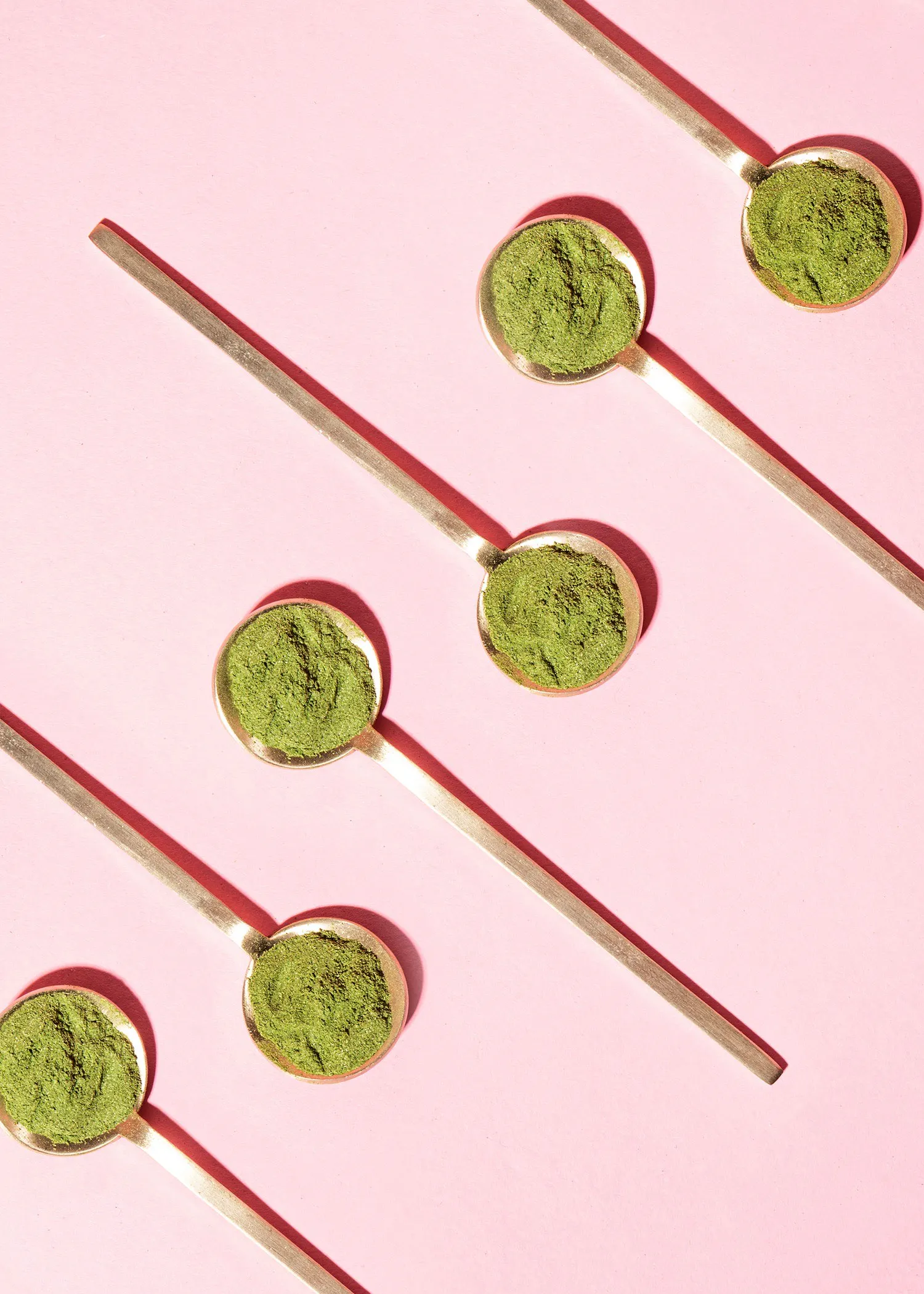 quatre cuillères remplies de poudre verte sur fond rose