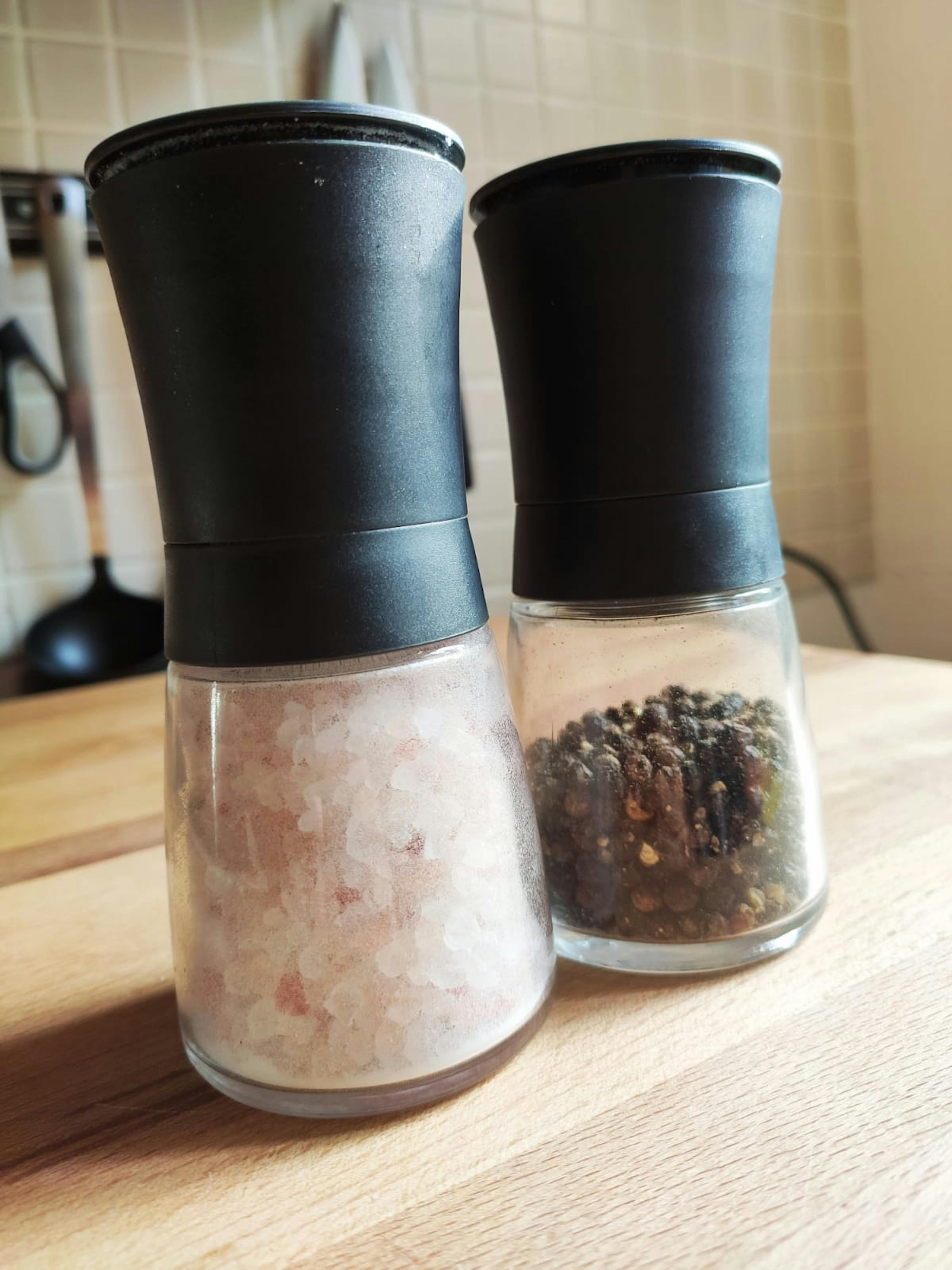 zwei Gewürzmühlen stehen auf einem Holztisch nebeneinander