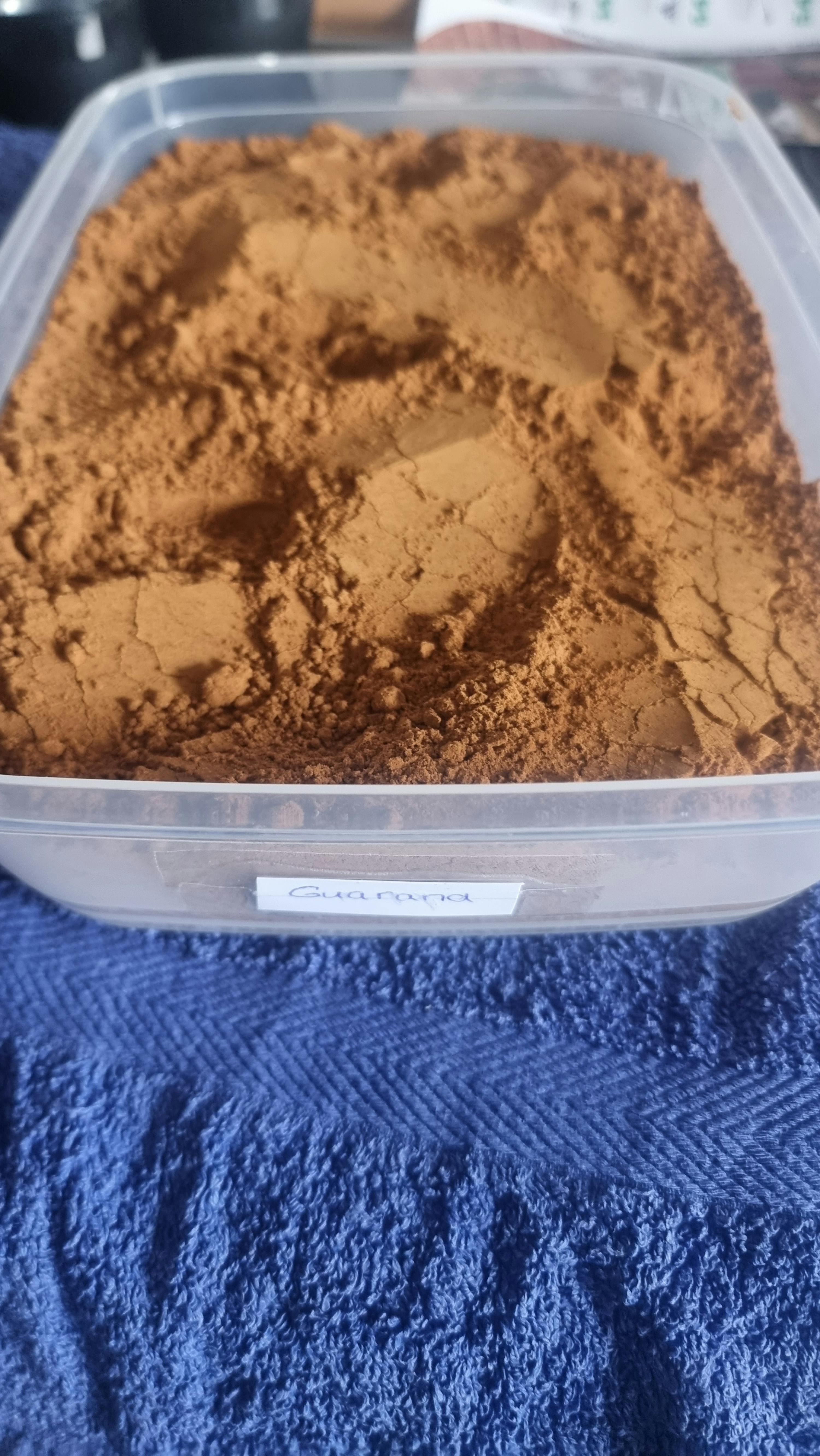 ein Plastikbehälter mit braunem Pulver steht auf einem blauen Handtuch