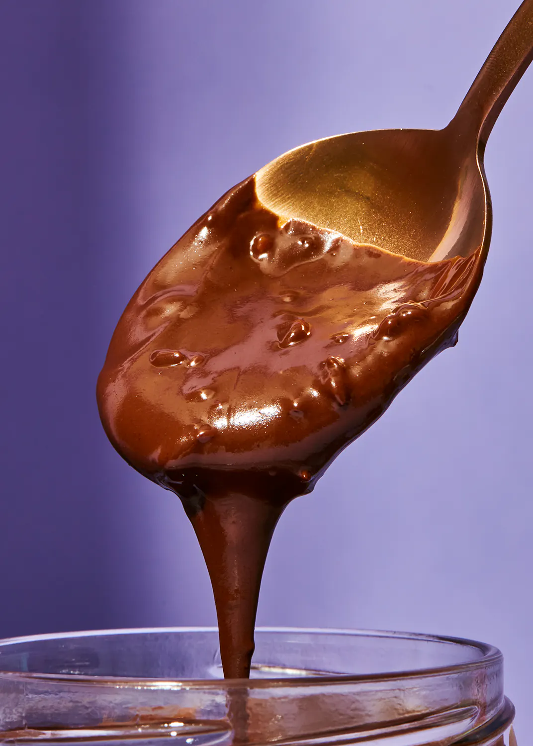 une cuillère remplie de sauce au chocolat coule d' un bocal en verre
