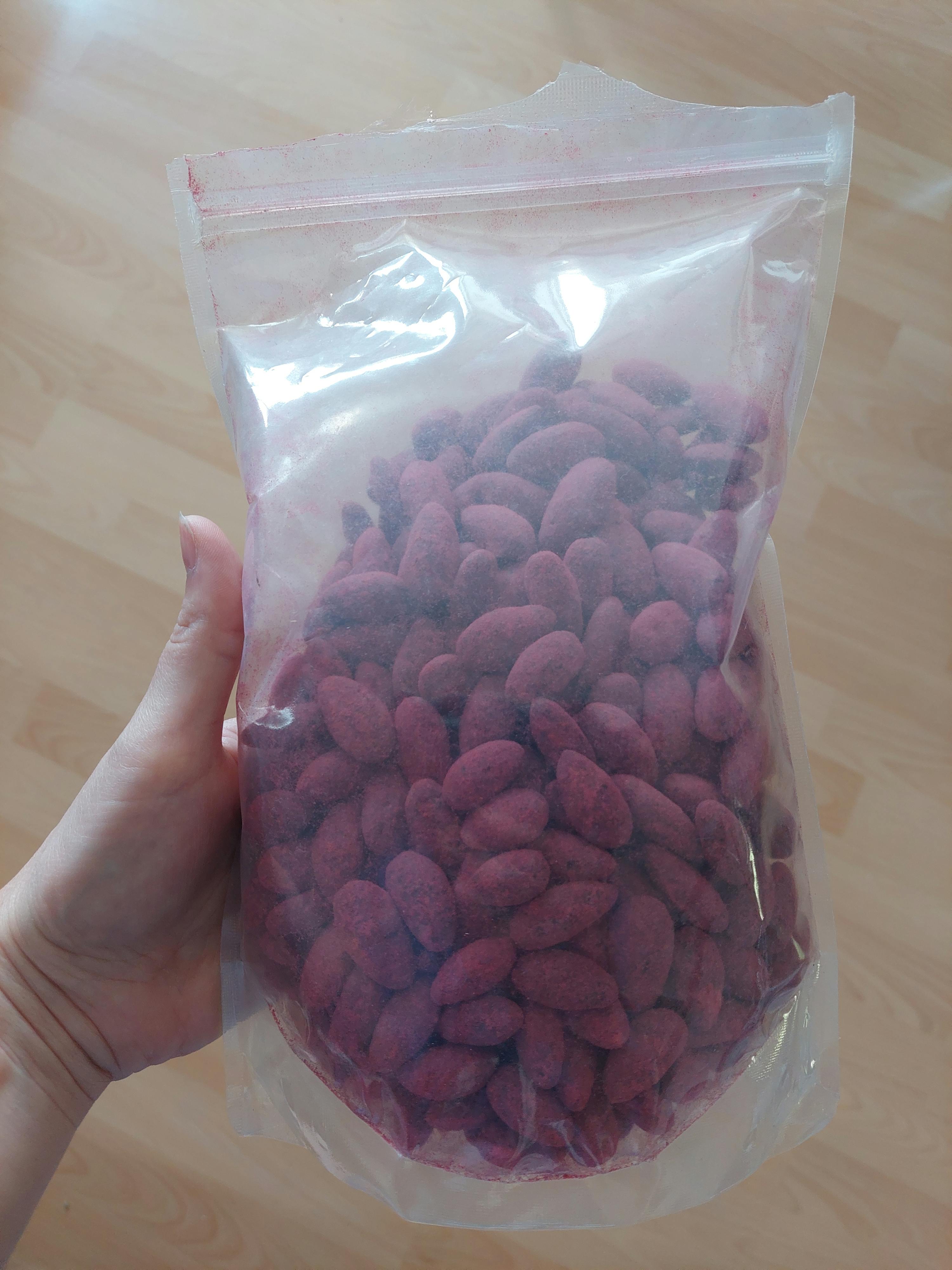 eine Person hält einen Plastikbeutel mit roten Mandeln darin