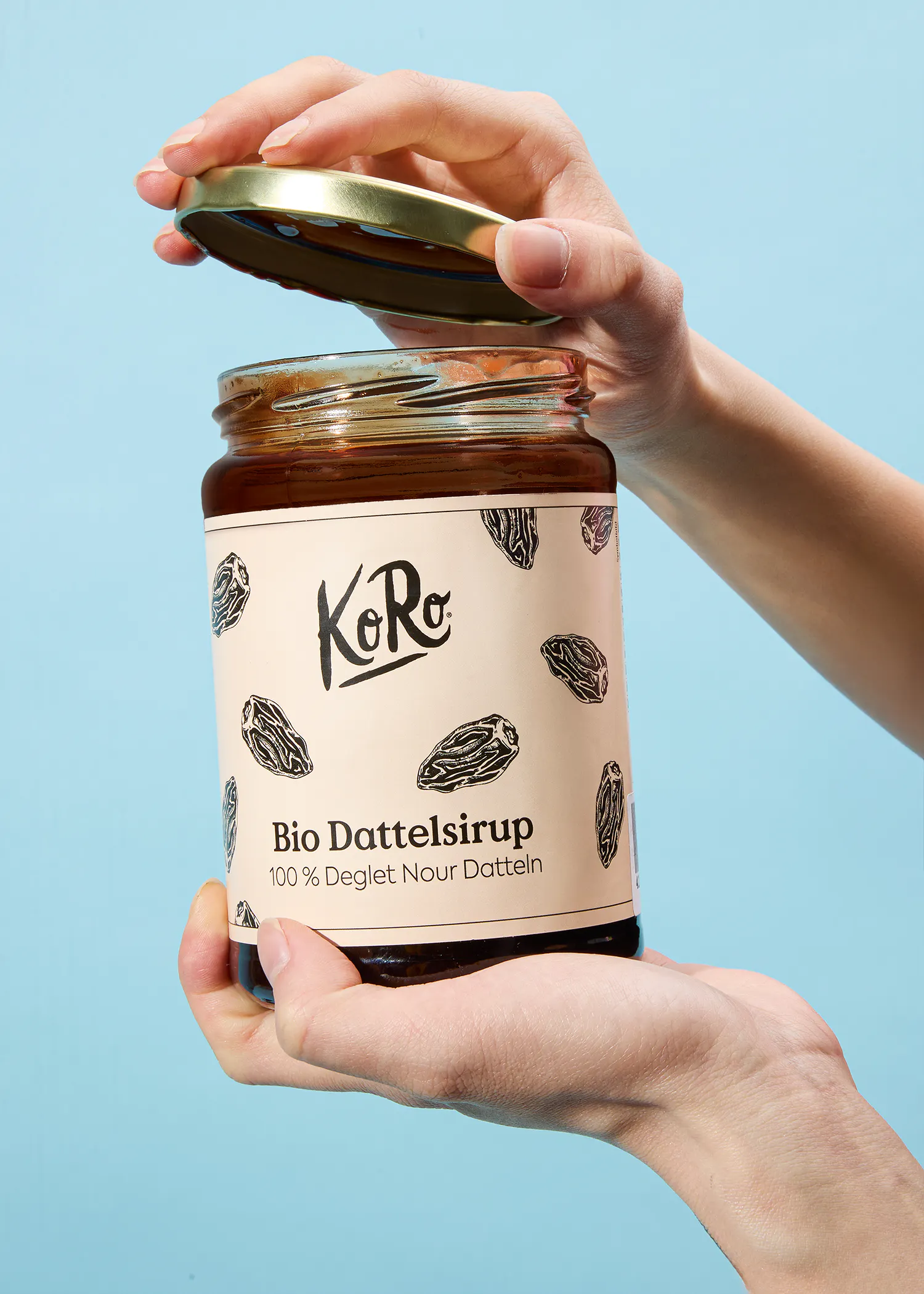 une personne tient un bocal de sirop de dattes bio koro