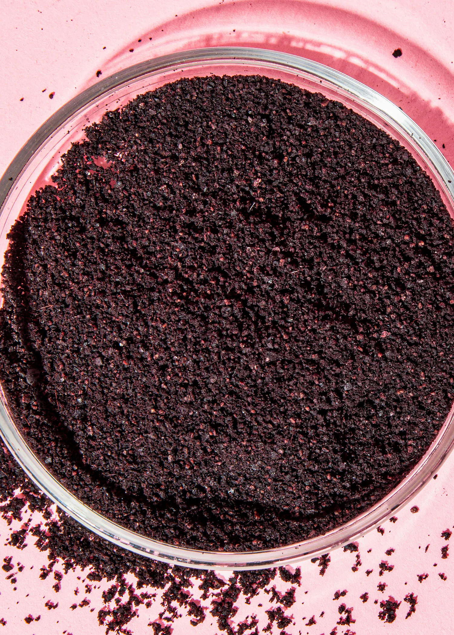 eine Nahaufnahme einer Glasschale mit schwarzem Pulver auf einem rosa Hintergrund