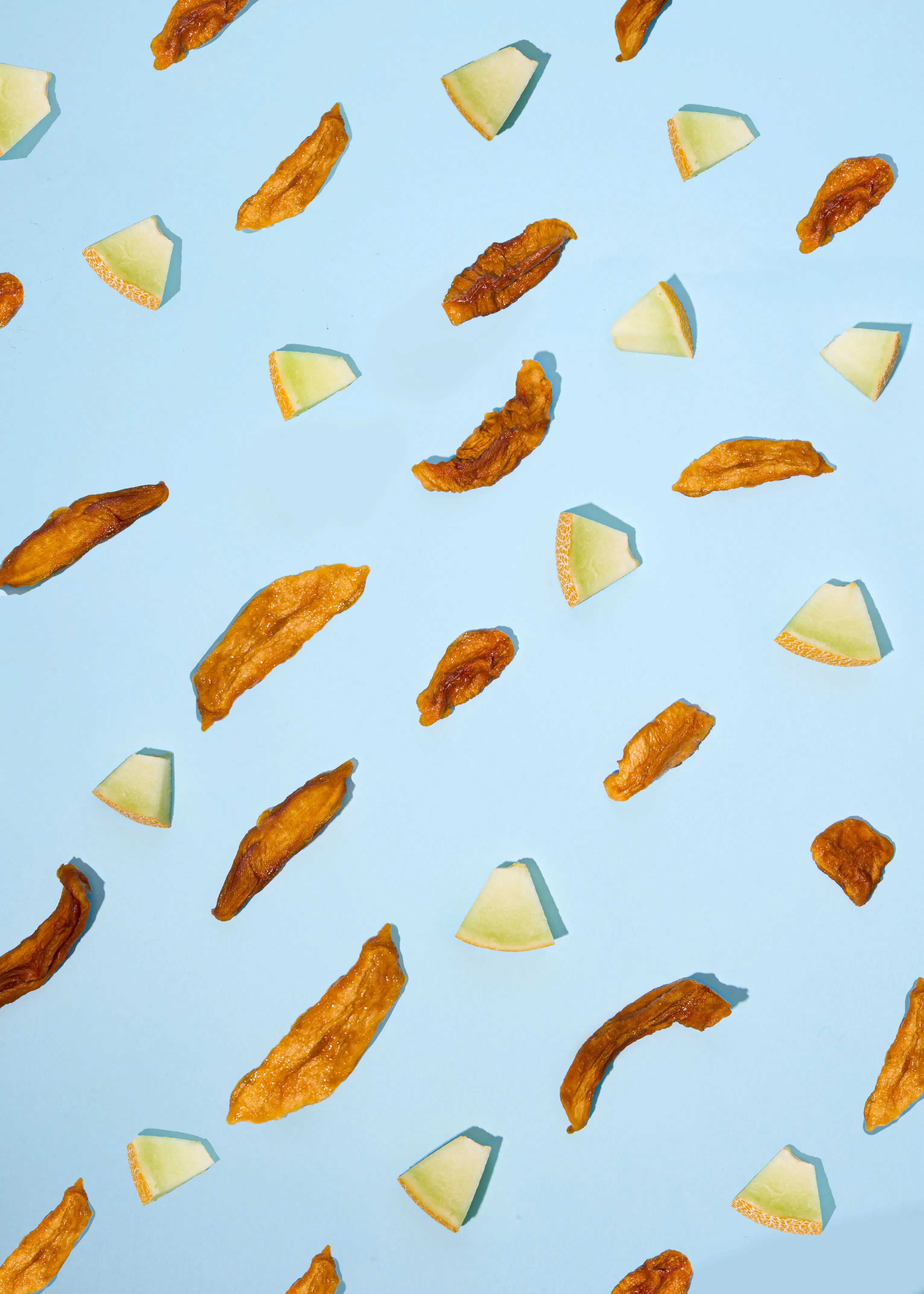 a pattern of dried mango slices and fresh cantaloupe wedges scattered on a light blue background.