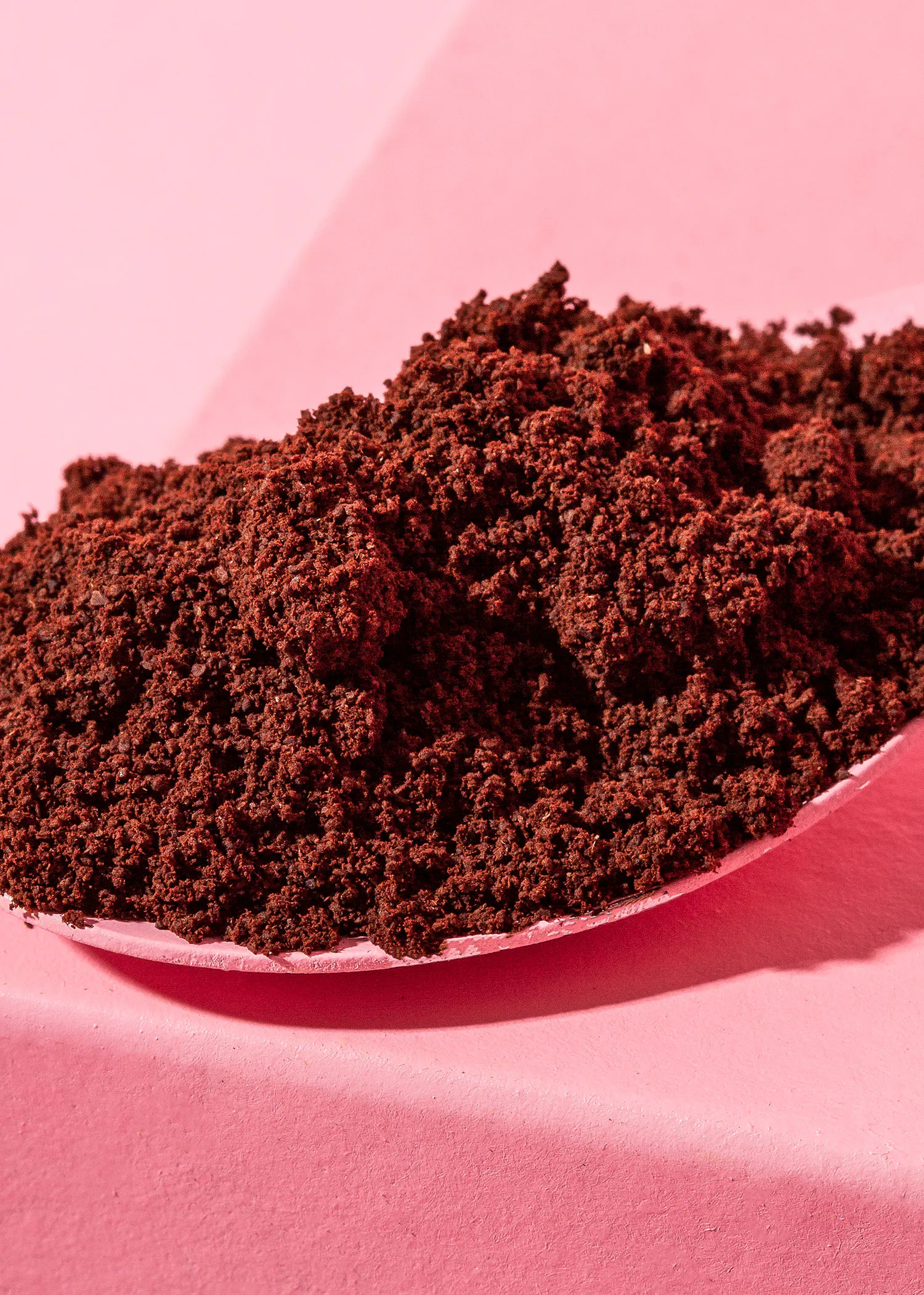 une cuillère remplie de poudre de café sur une table rose