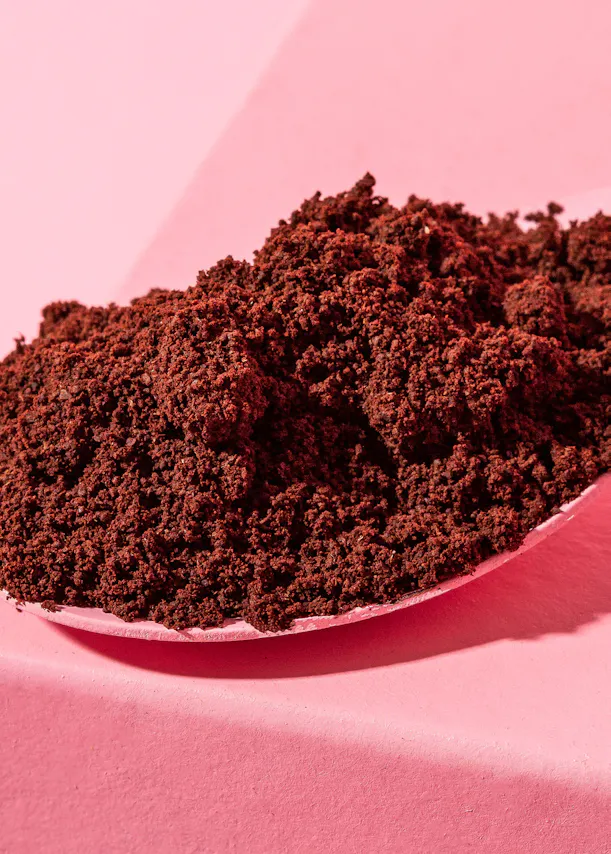 une cuillère remplie de poudre de café sur une table rose