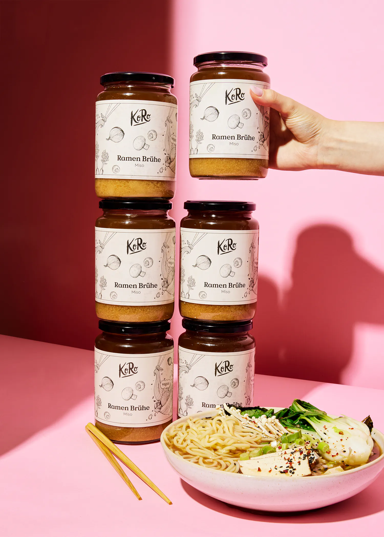 une personne tient un pot de ramen broth à côté d' un bol de nouilles