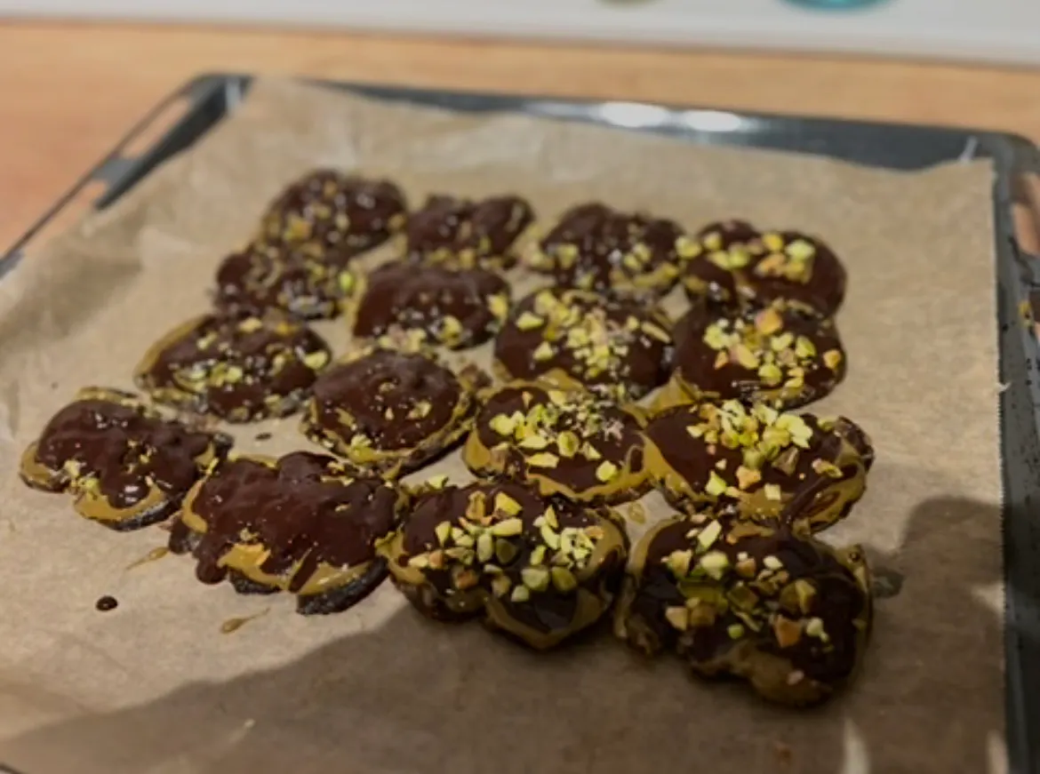 mit schokolade überzogene kekse mit gehackten pistazien auf einem backblech.