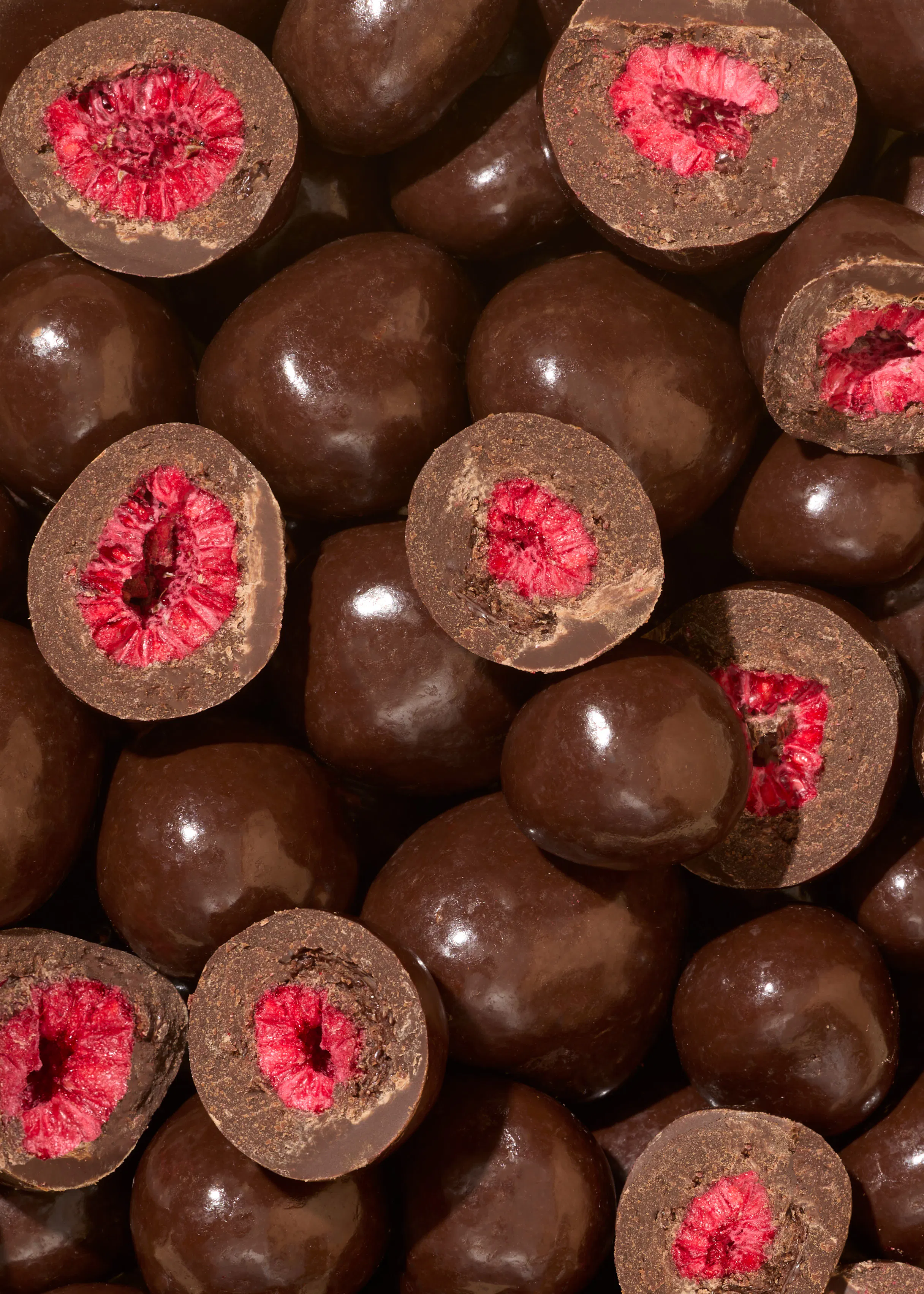 a pile of chocolate covered raspberries that have been cut in half