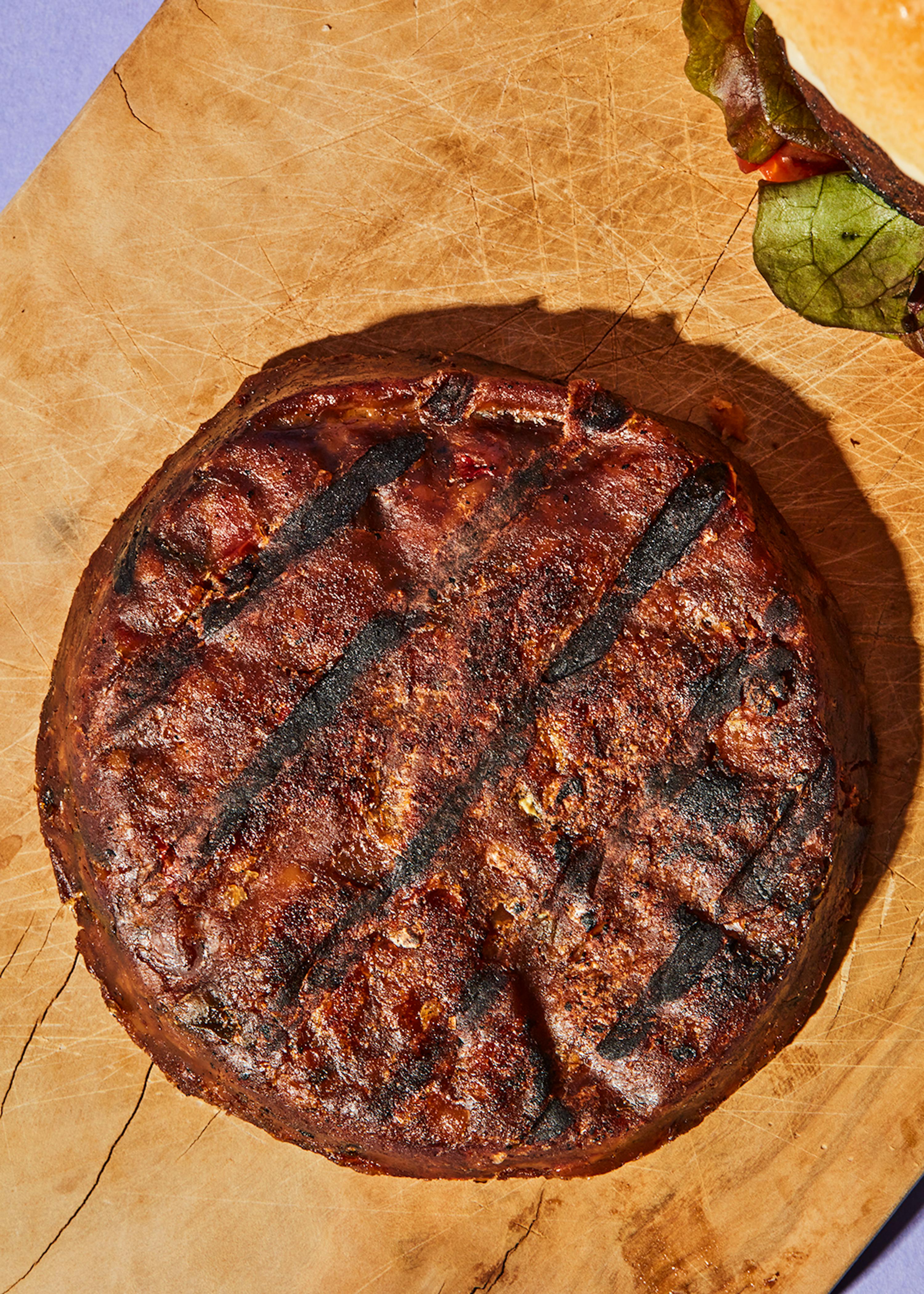 una hamburguesa a la parrilla está sobre una tabla de cortar de madera