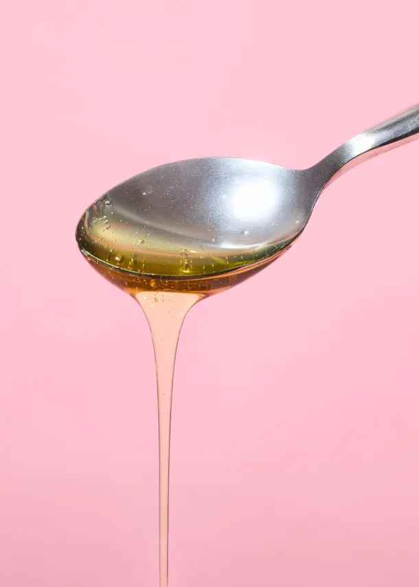 Honig fließt aus einem Löffel auf einem rosa Hintergrund