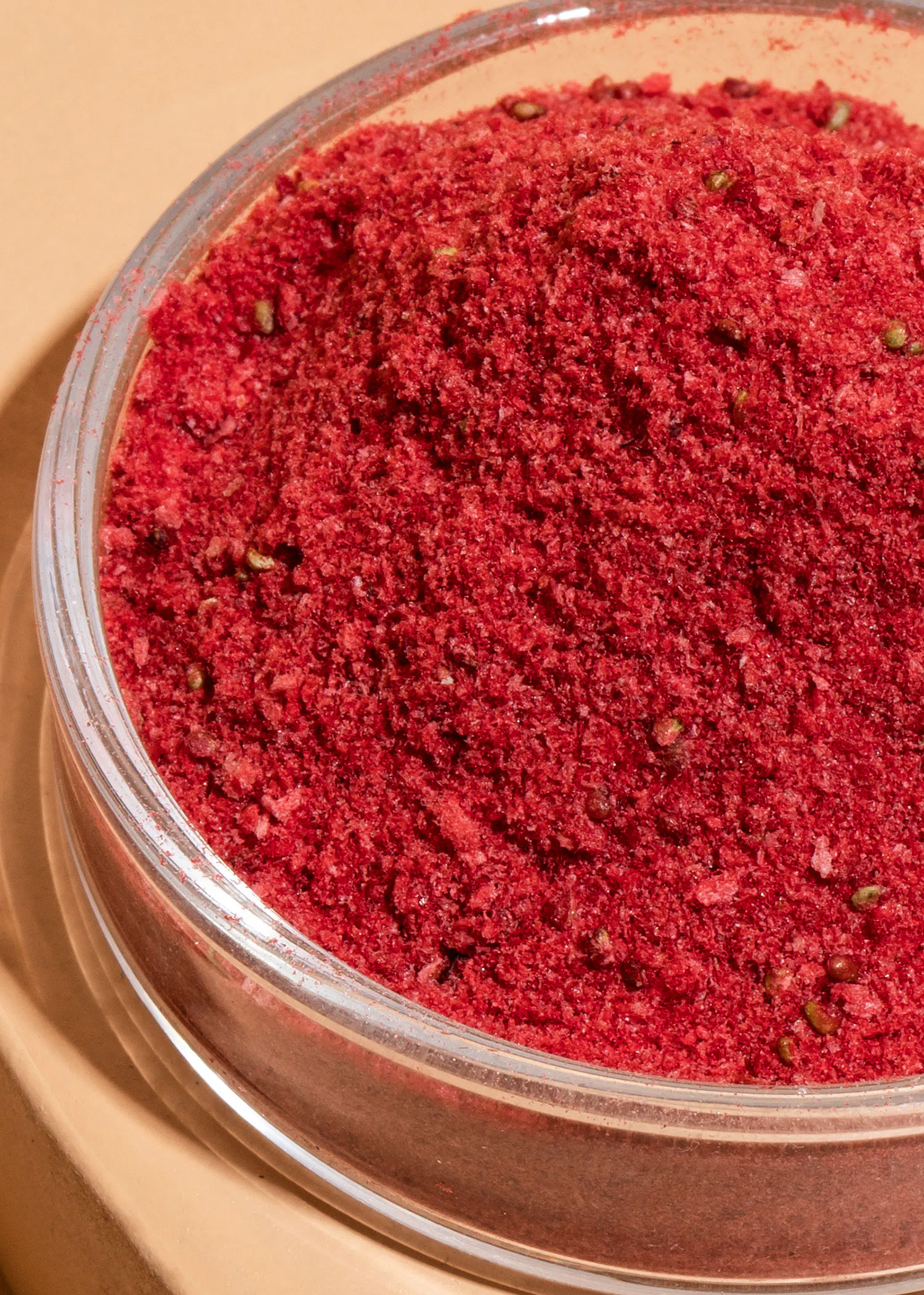 un bol en verre rempli de poudre rouge avec des graines vertes