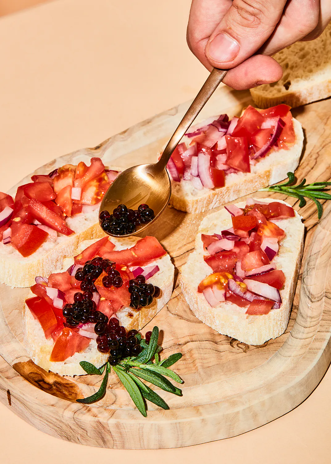 una persona agrega caviar a un sándwich con tomates y cebollas