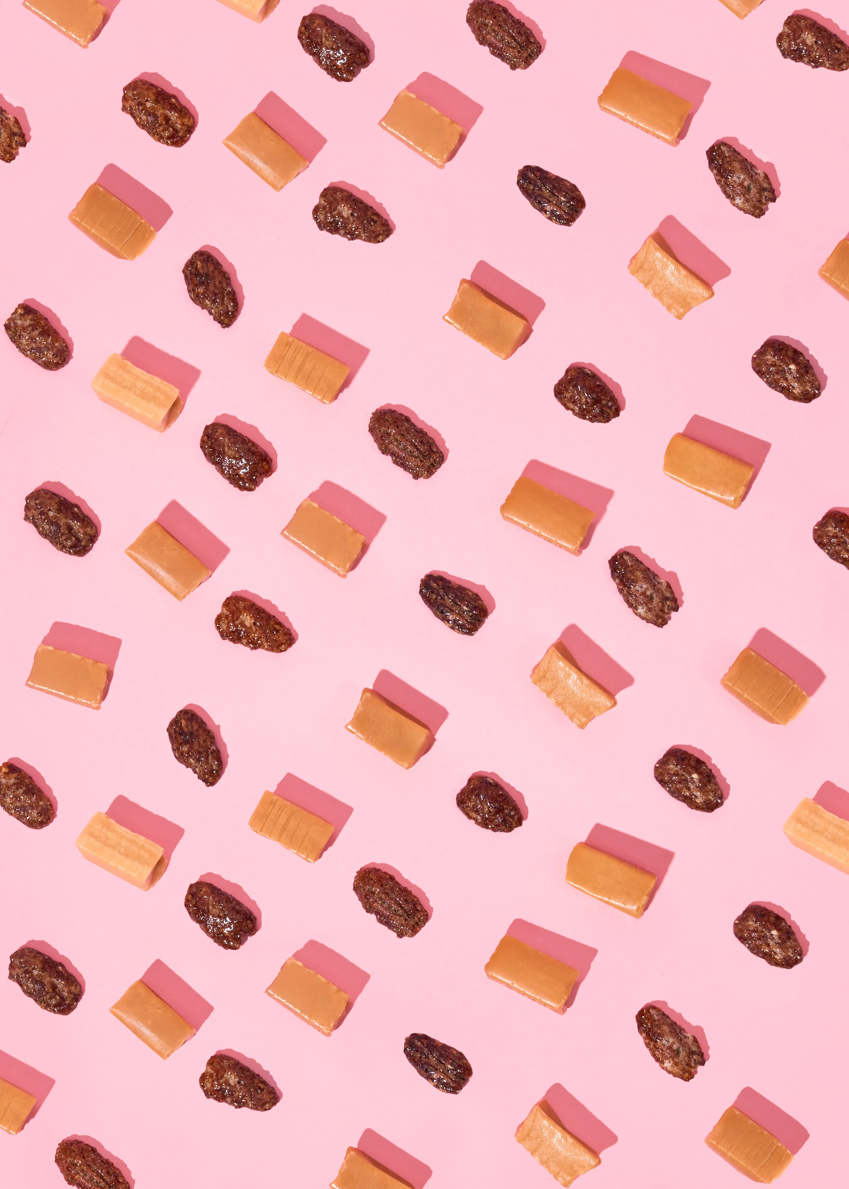 un motif répétitif de bonbons au caramel et de dattes ou de noix sur un fond rose avec des ombres.