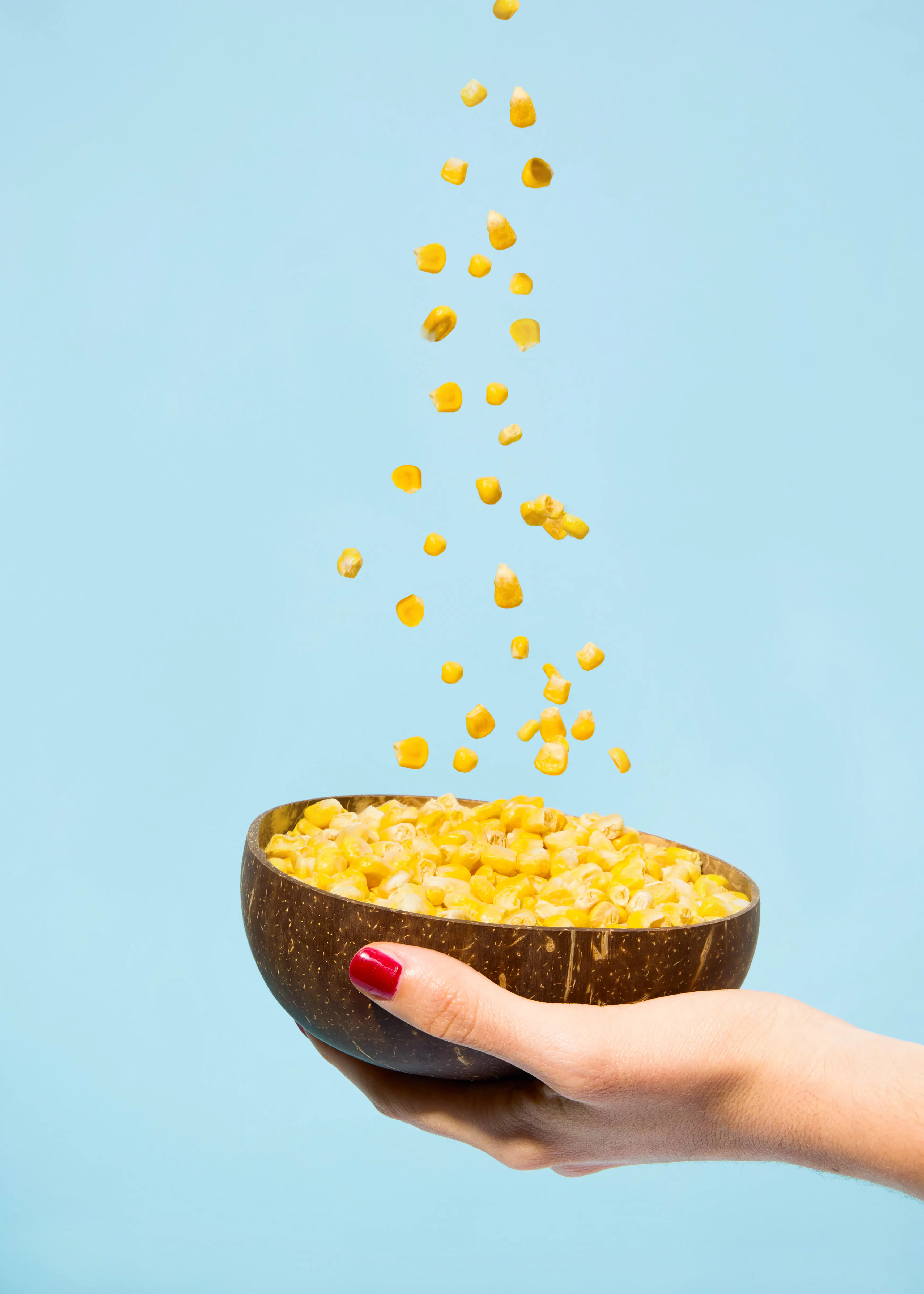 a hand with red nail polish holds a bowl of corn