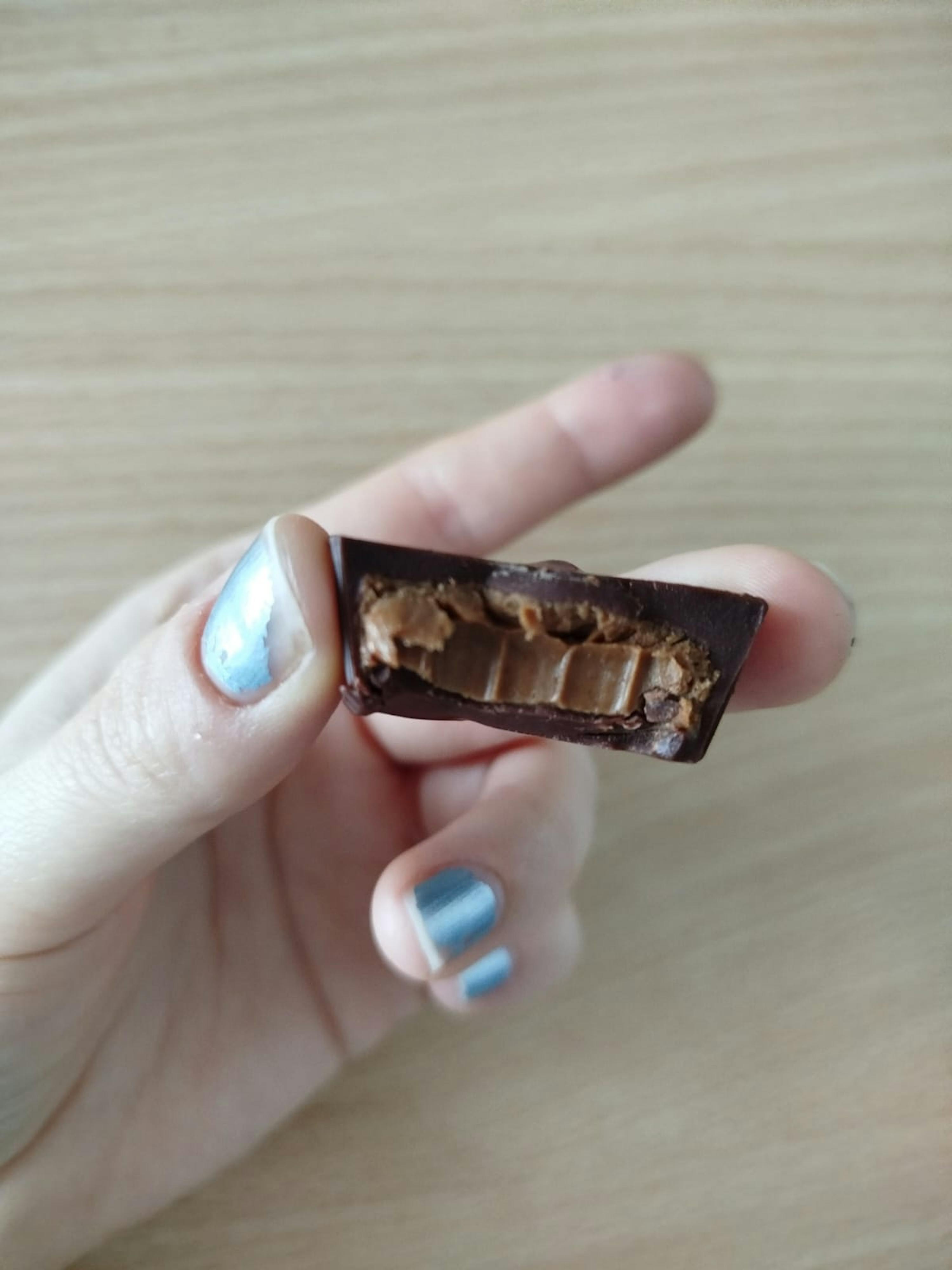 a person with blue nail polish is holding a piece of chocolate