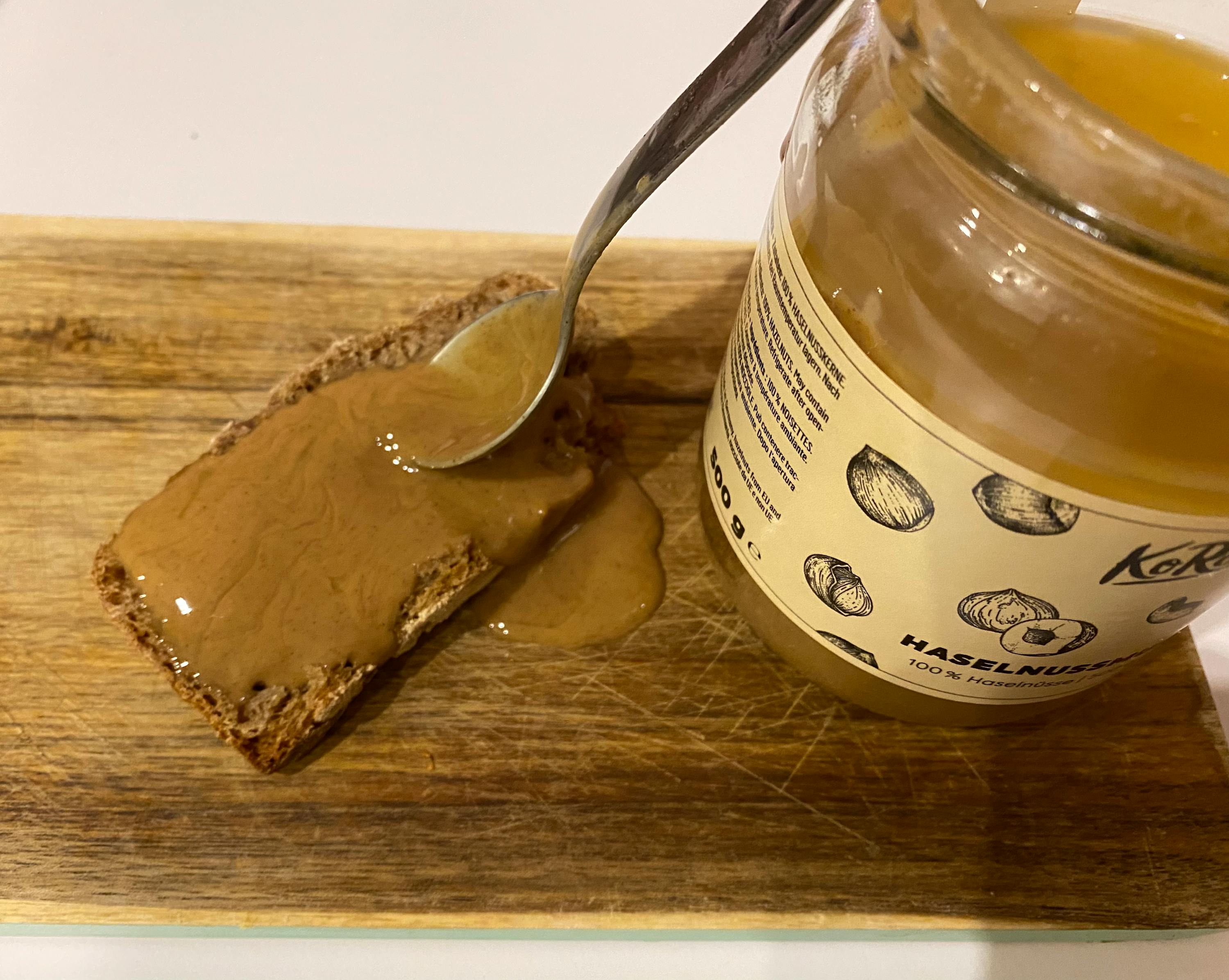 un barattolo di burro di nocciole è accanto a un pezzo di pane su un tagliere di legno