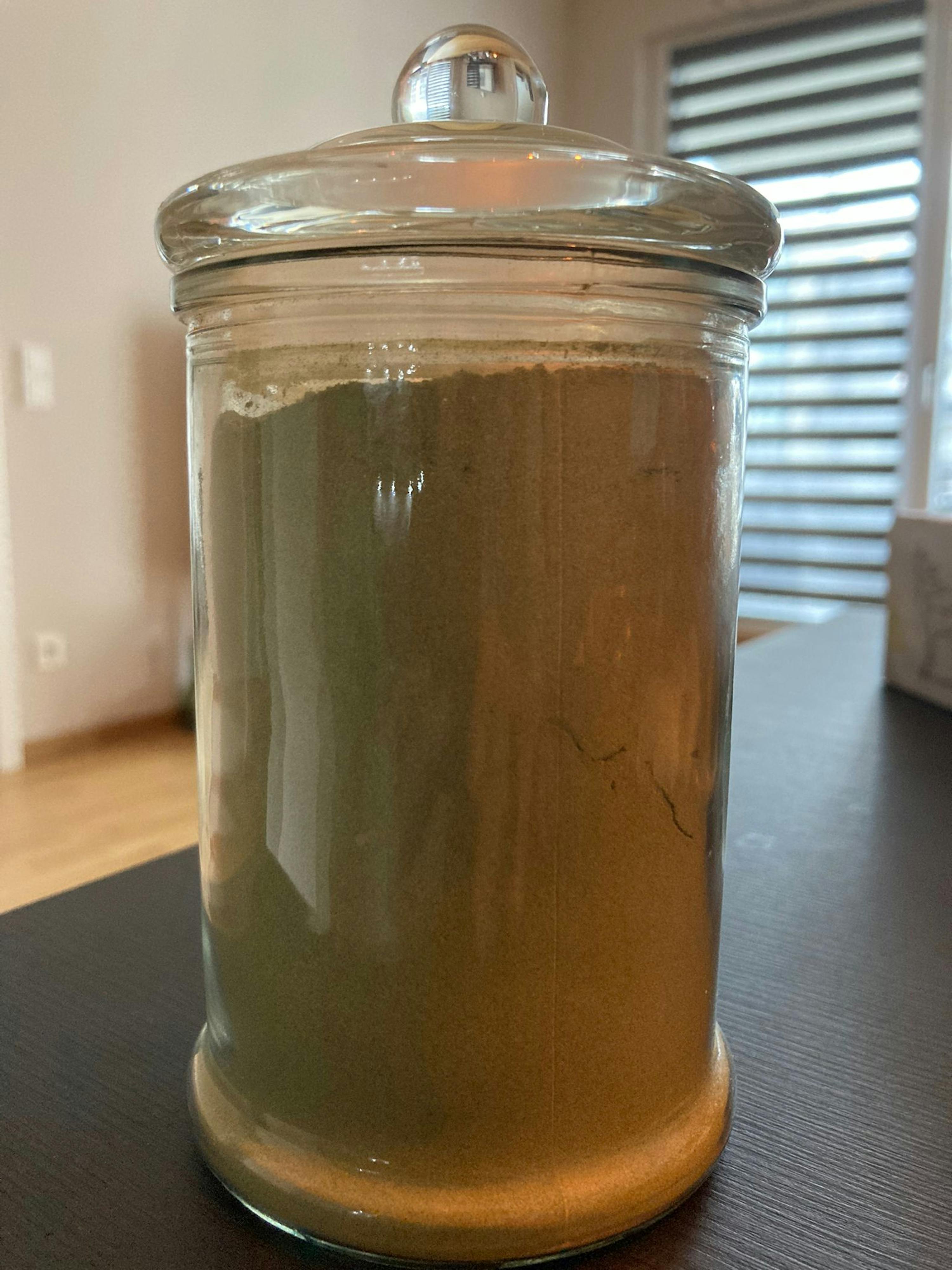 un bocal en verre rempli de poudre verte est sur une table