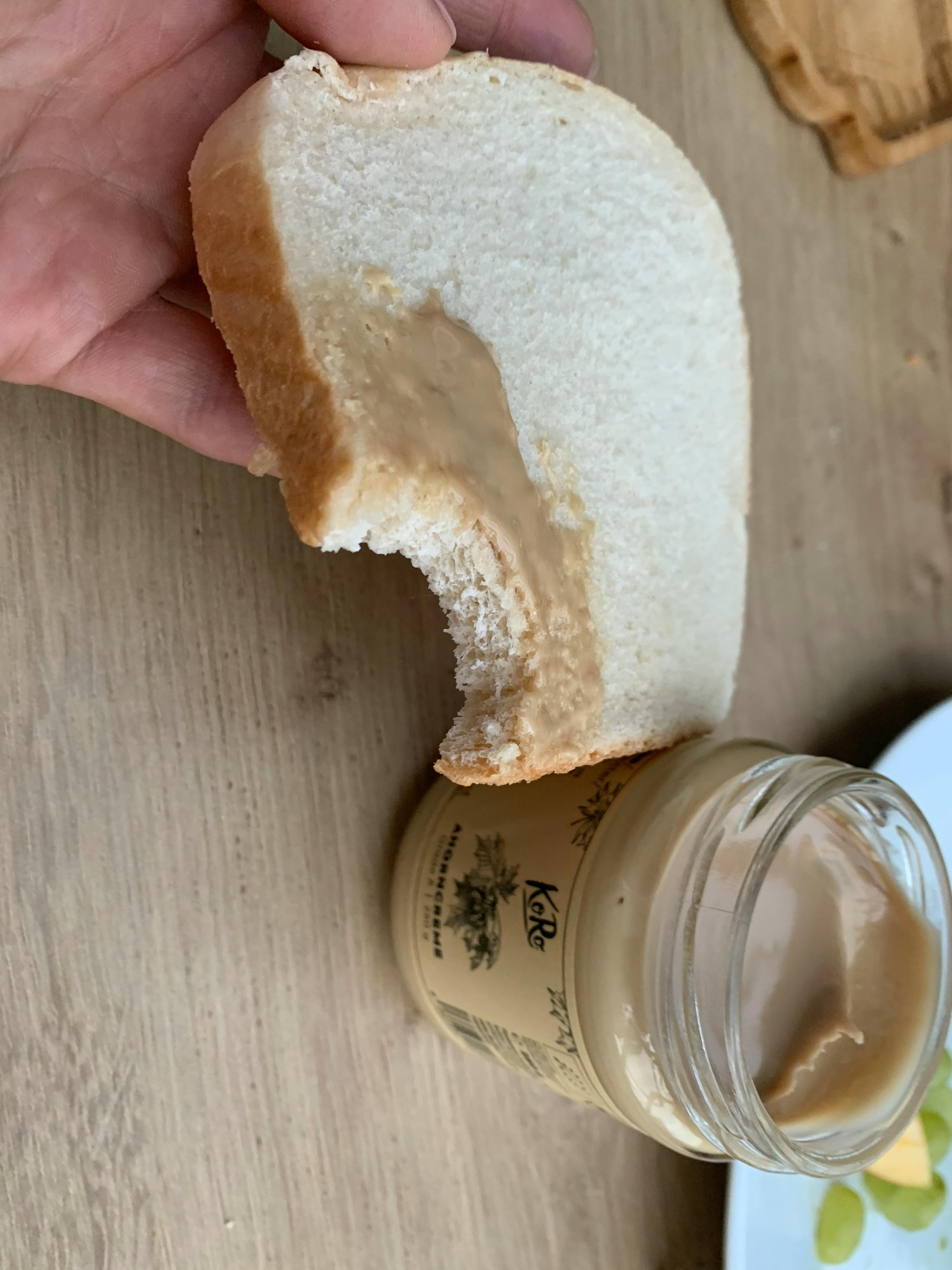 eine Hand hält ein Stück Brot neben einem Krug Kokosnusscreme