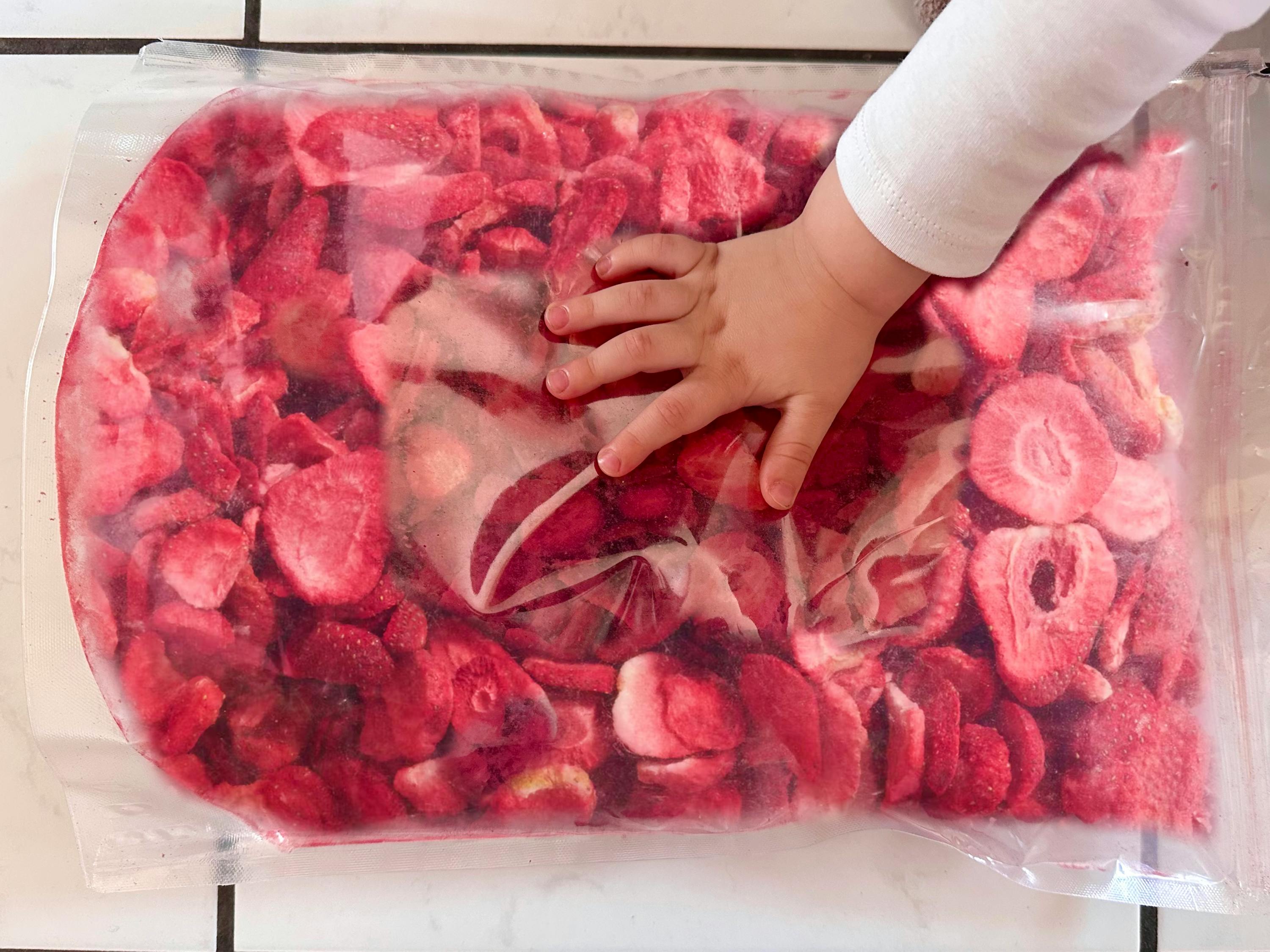 a child 's hand is reaching into a bag of frozen strawberries