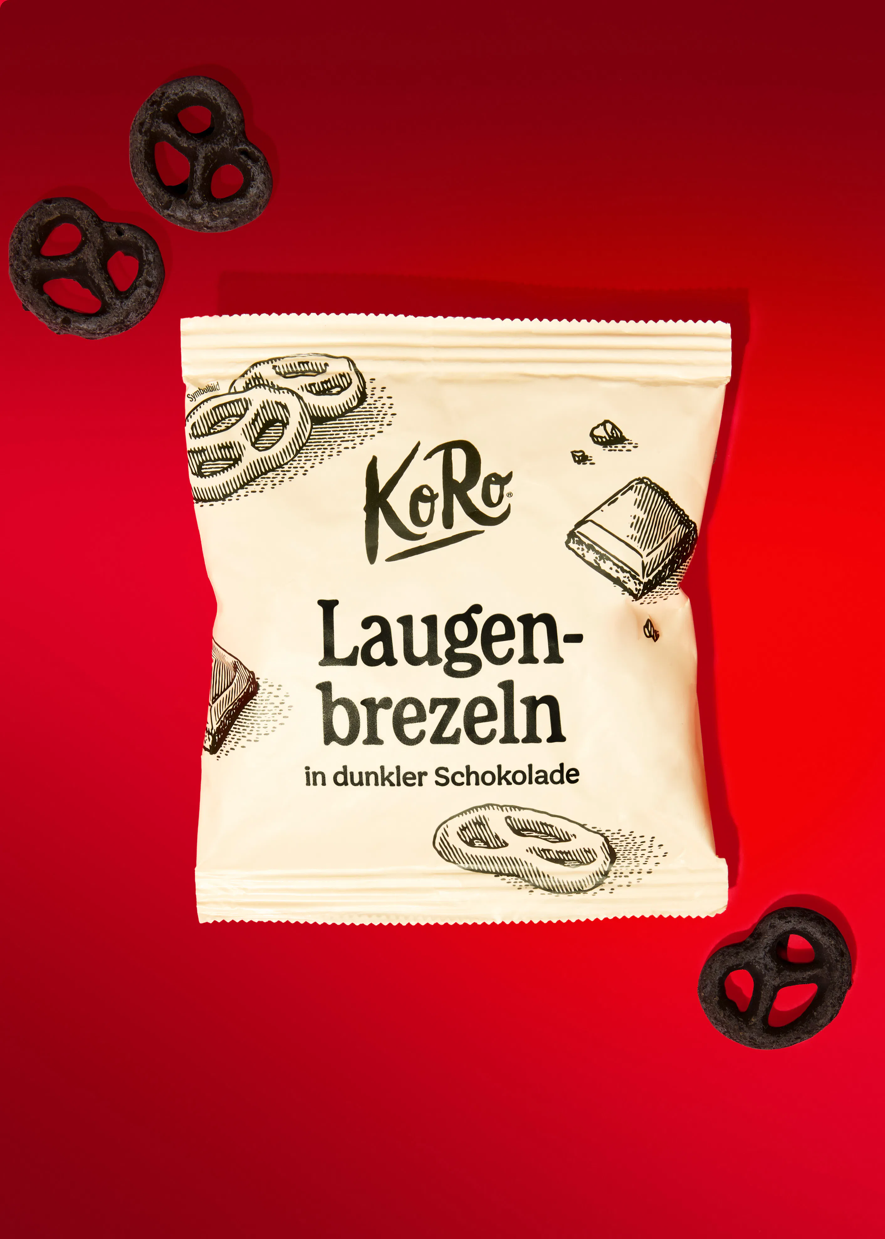paquet de bretzels enrobés de chocolat noir de la marque koro posé sur un fond rouge vif avec quelques bretzels éparpillés autour.