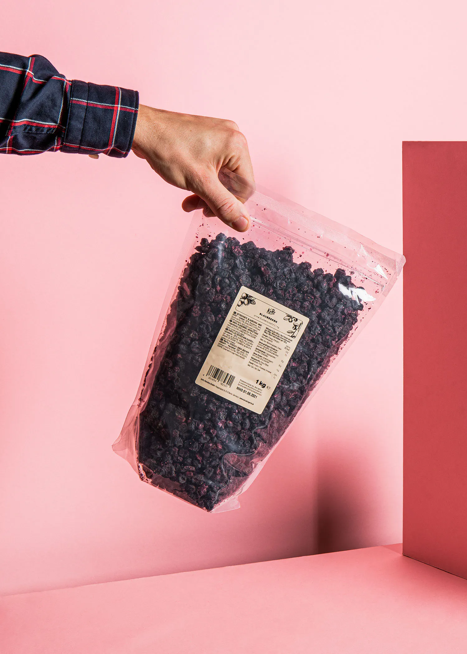 une personne tient un sac de myrtilles séchées sur fond rose