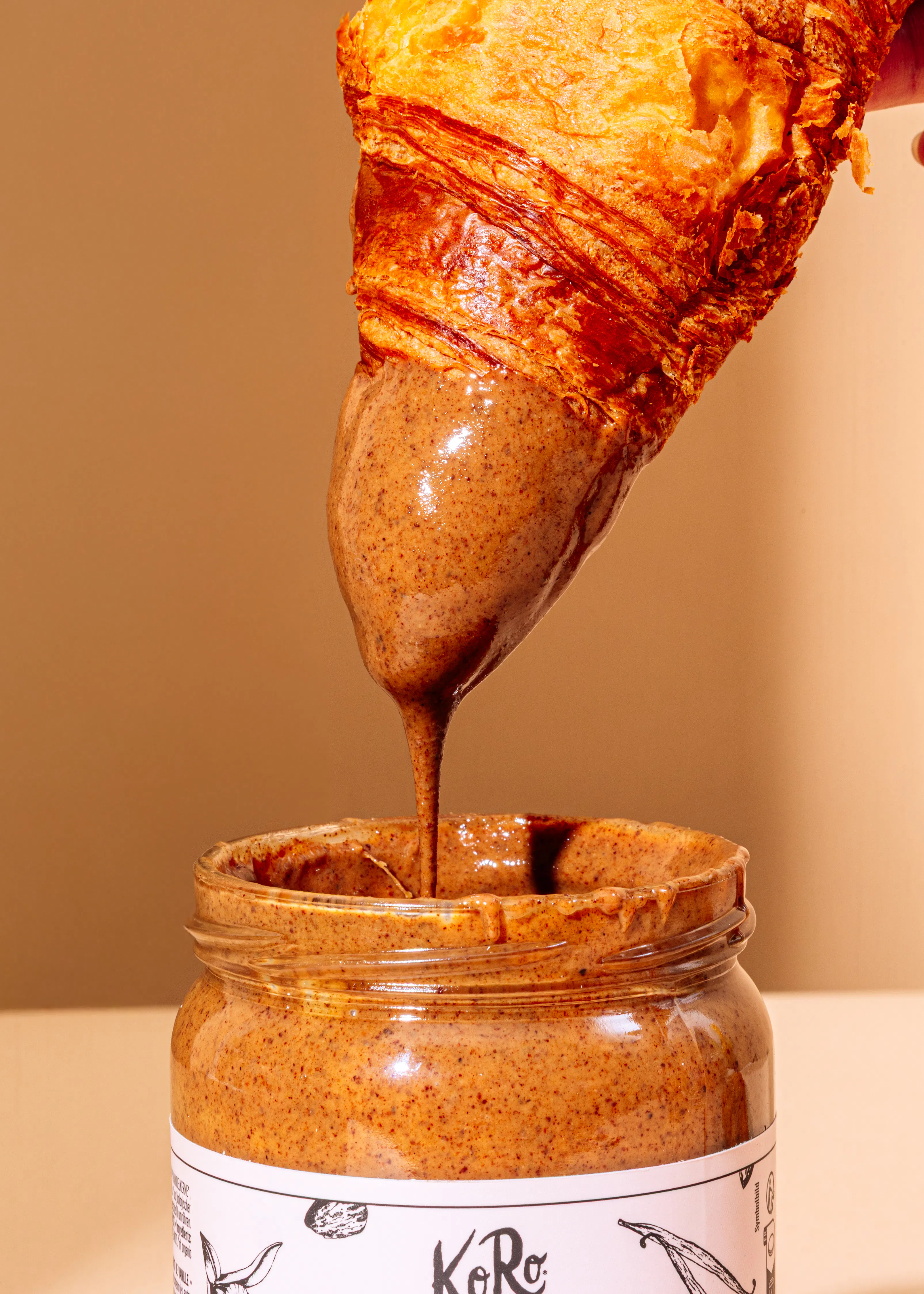 eine Person gießt Erdnussbutter auf einen Croissant in ein Glas