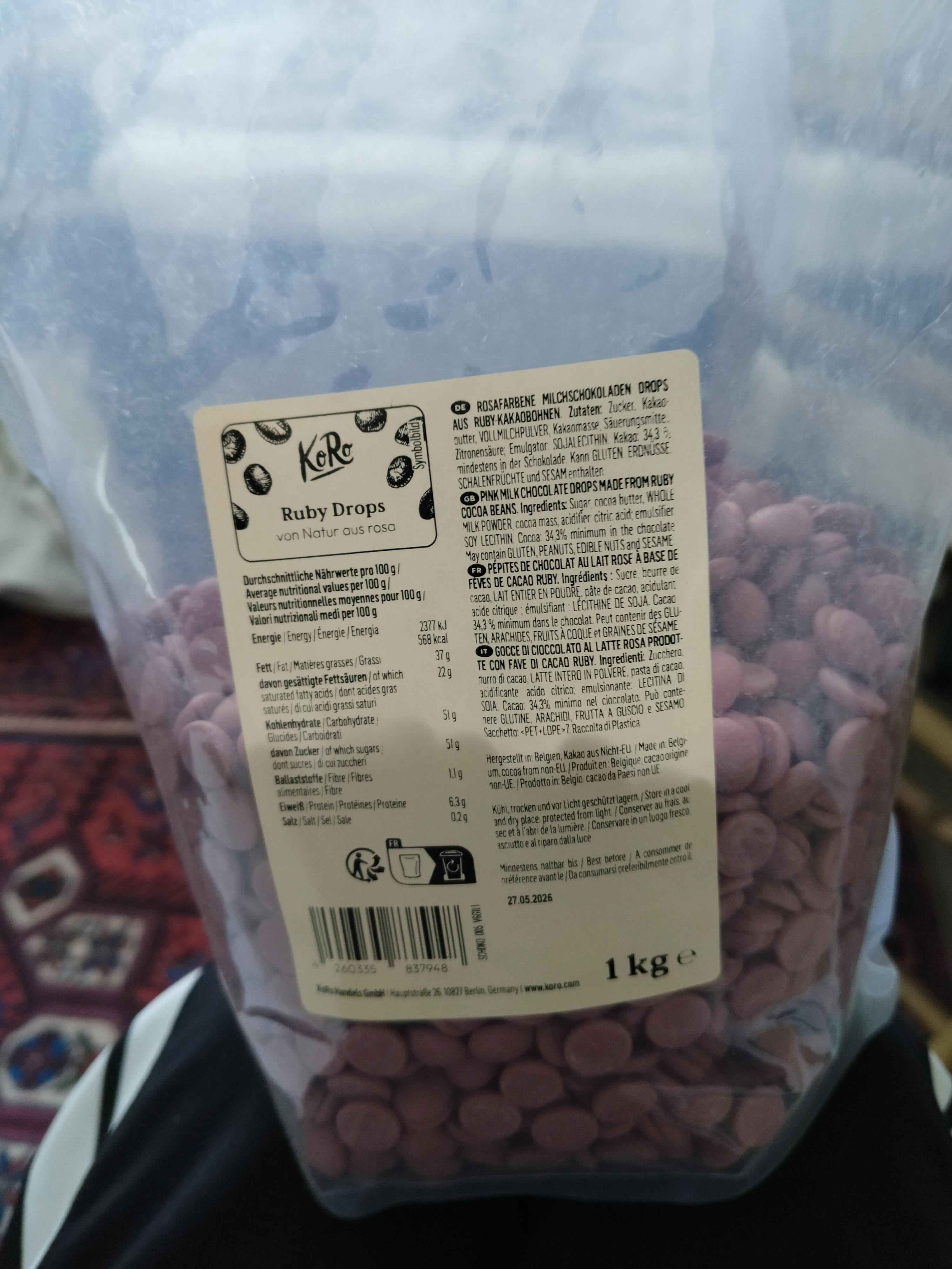 eine durchsichtige plastiktüte, gefüllt mit kleinen, rosafarbenen ruby-schokoladendrops, mit einem etikett, das den markennamen 'koro ruby drops' und nährwertinformationen zeigt.