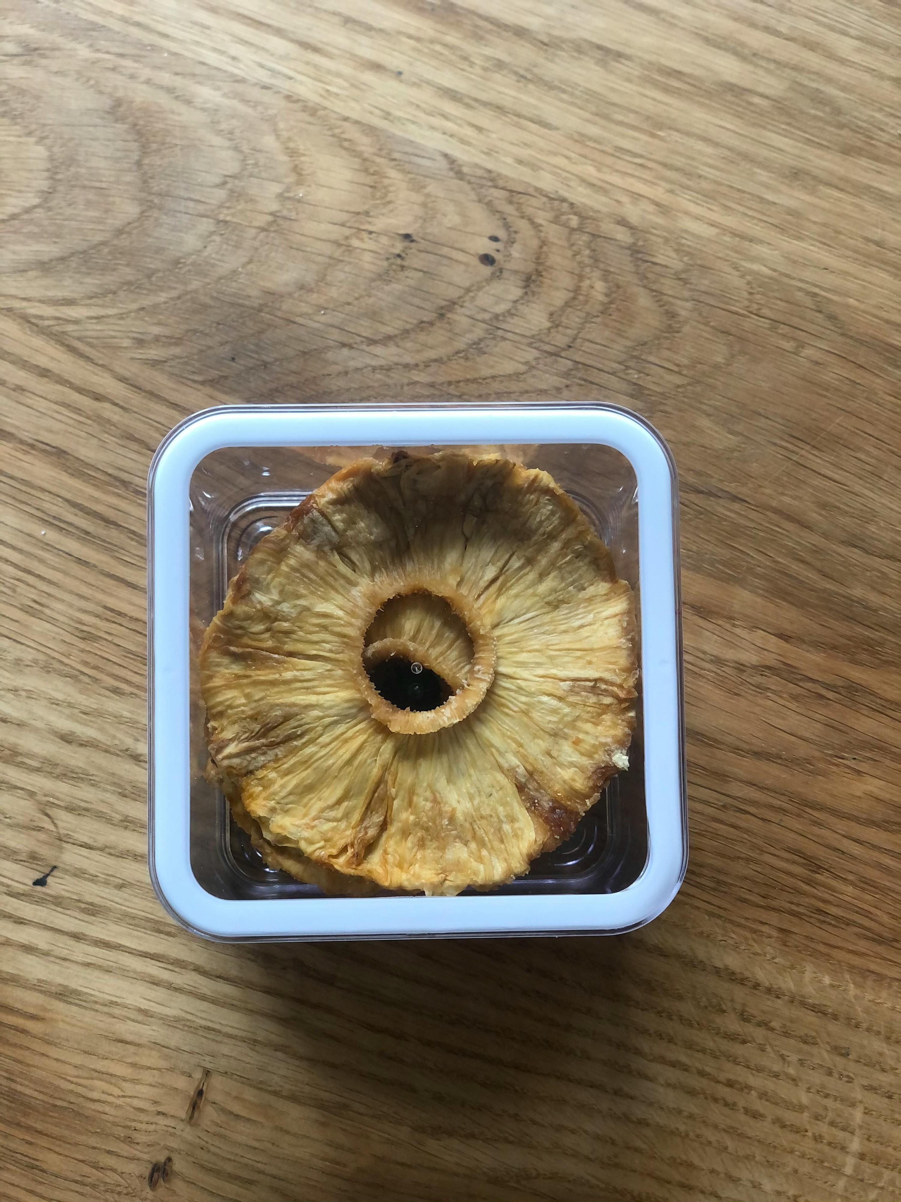 eine Ananasscheibe liegt in einem Plastikbehälter auf einem Holztisch