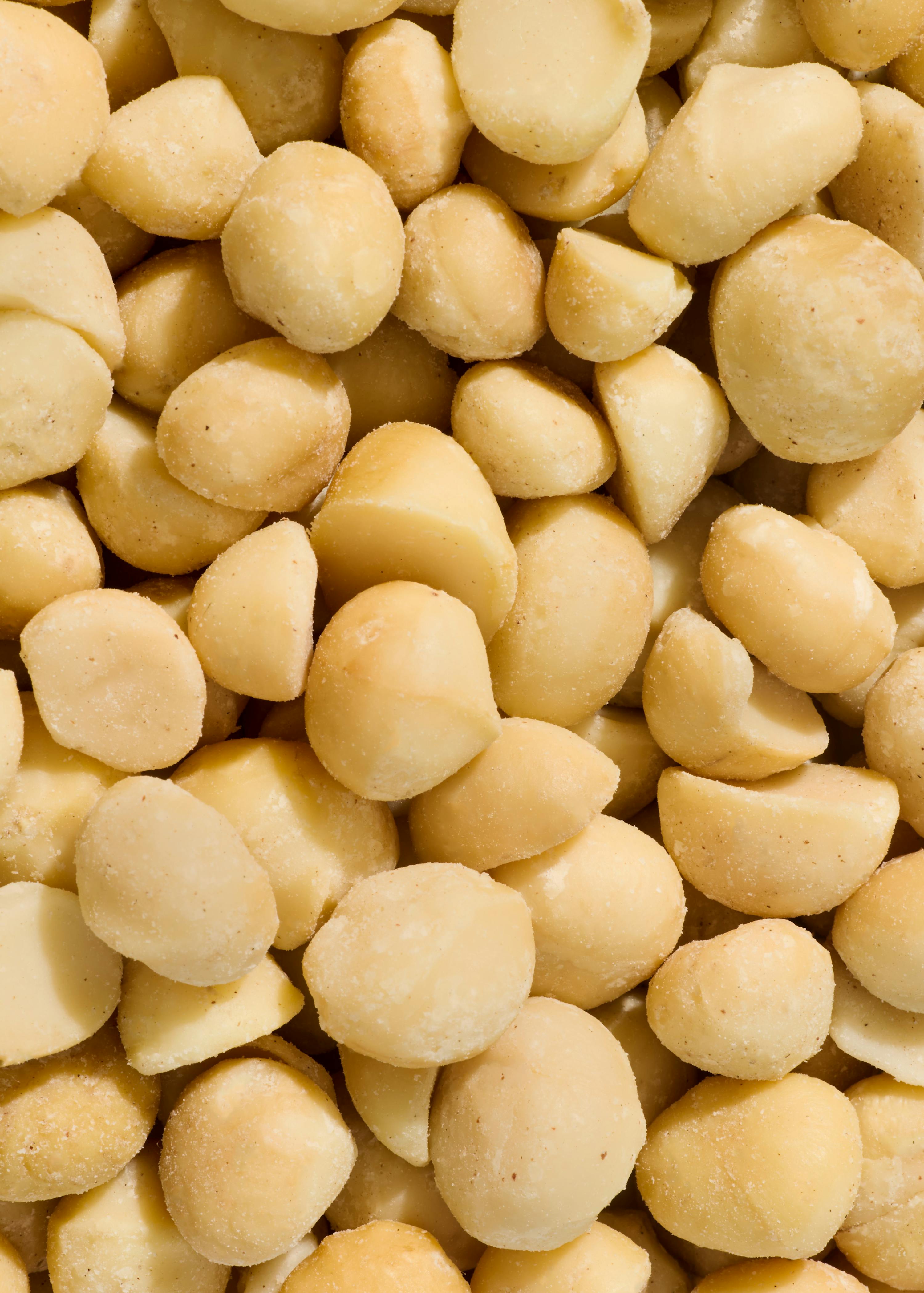 un primo piano di noci di macadamia intere e tagliate a metà, di colore giallo chiaro e leggermente testurizzate.
