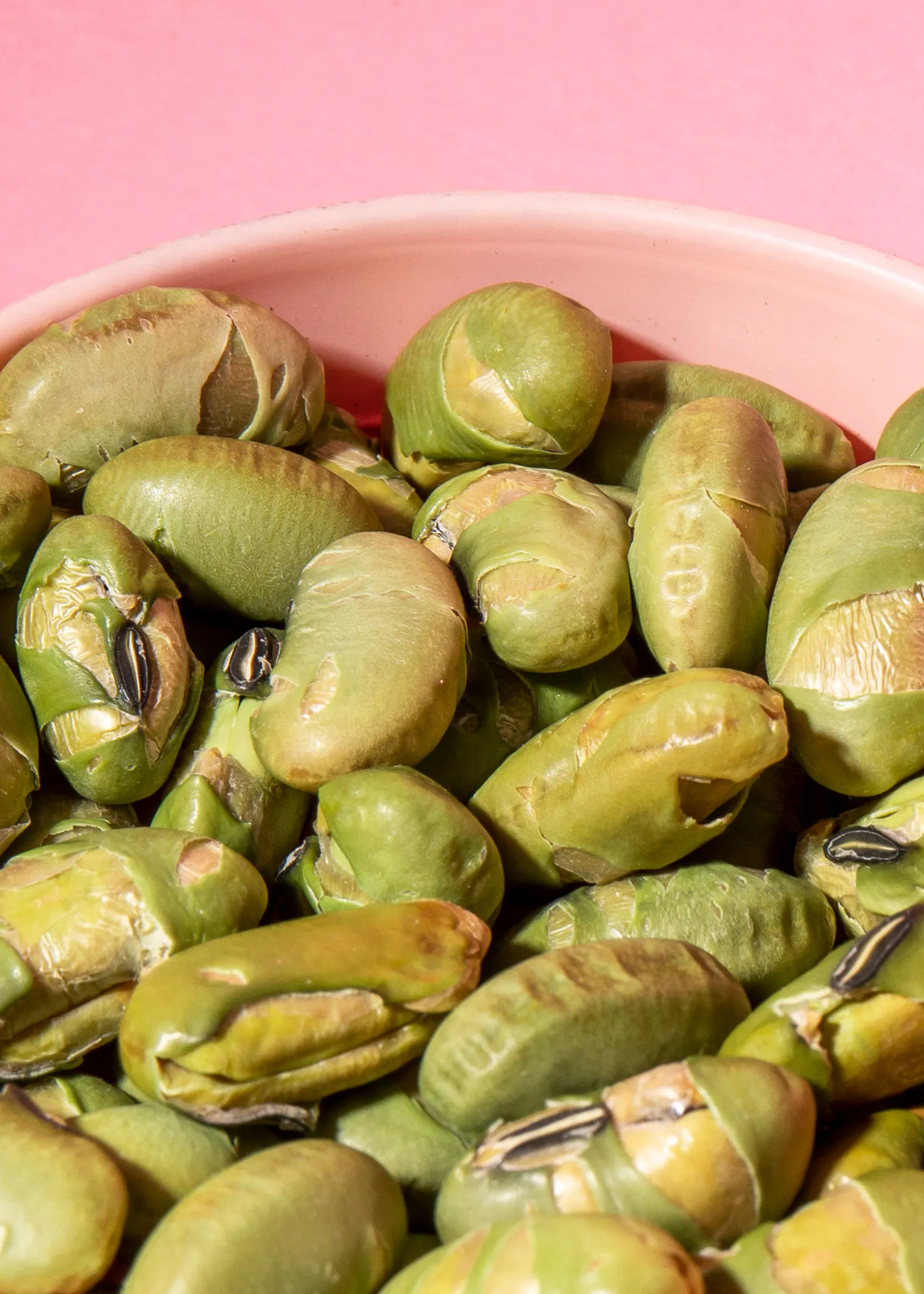 eine rosa Schüssel gefüllt mit grünen Bohnen auf einem rosa Hintergrund