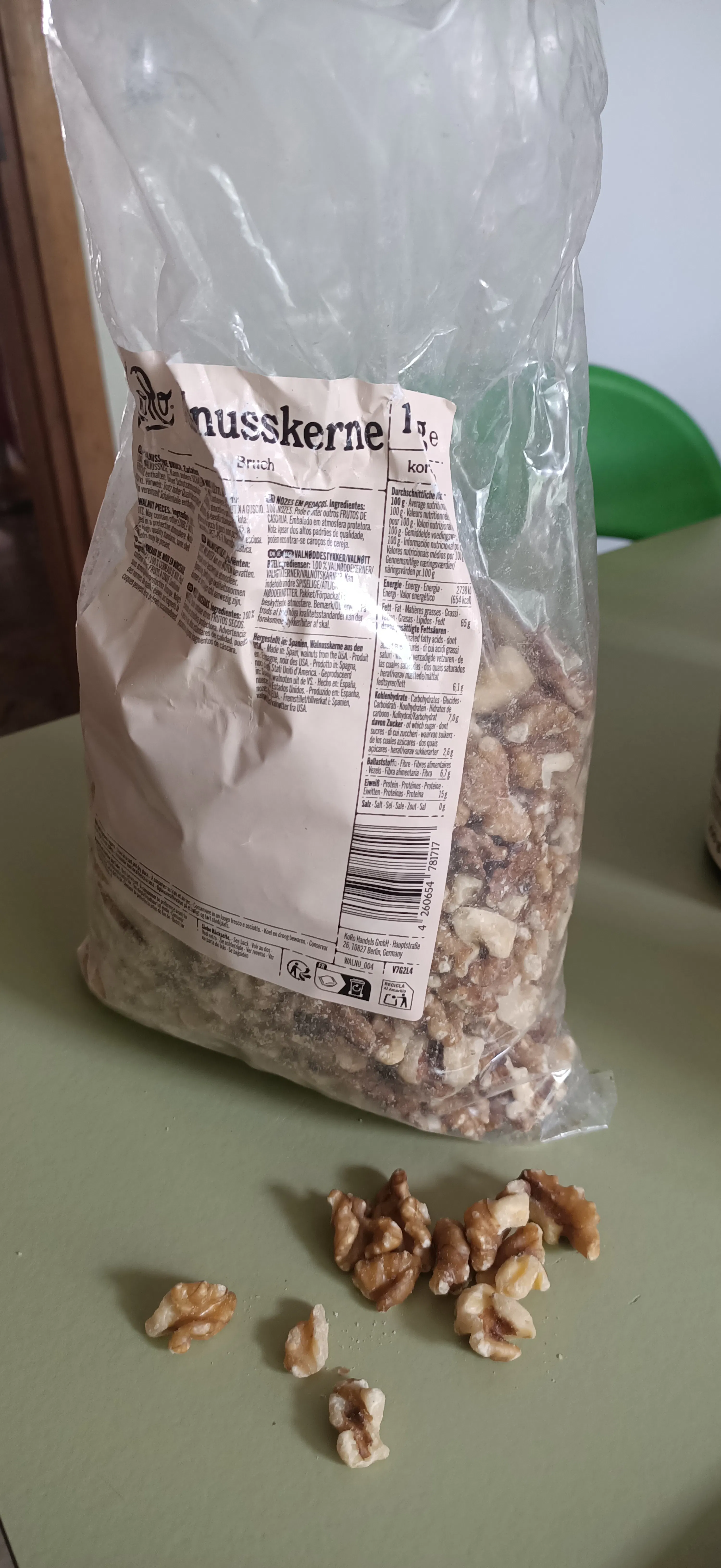a clear plastic bag of walnut kernels labeled 'nusskerne' sits on a green surface with several walnuts spilled out.