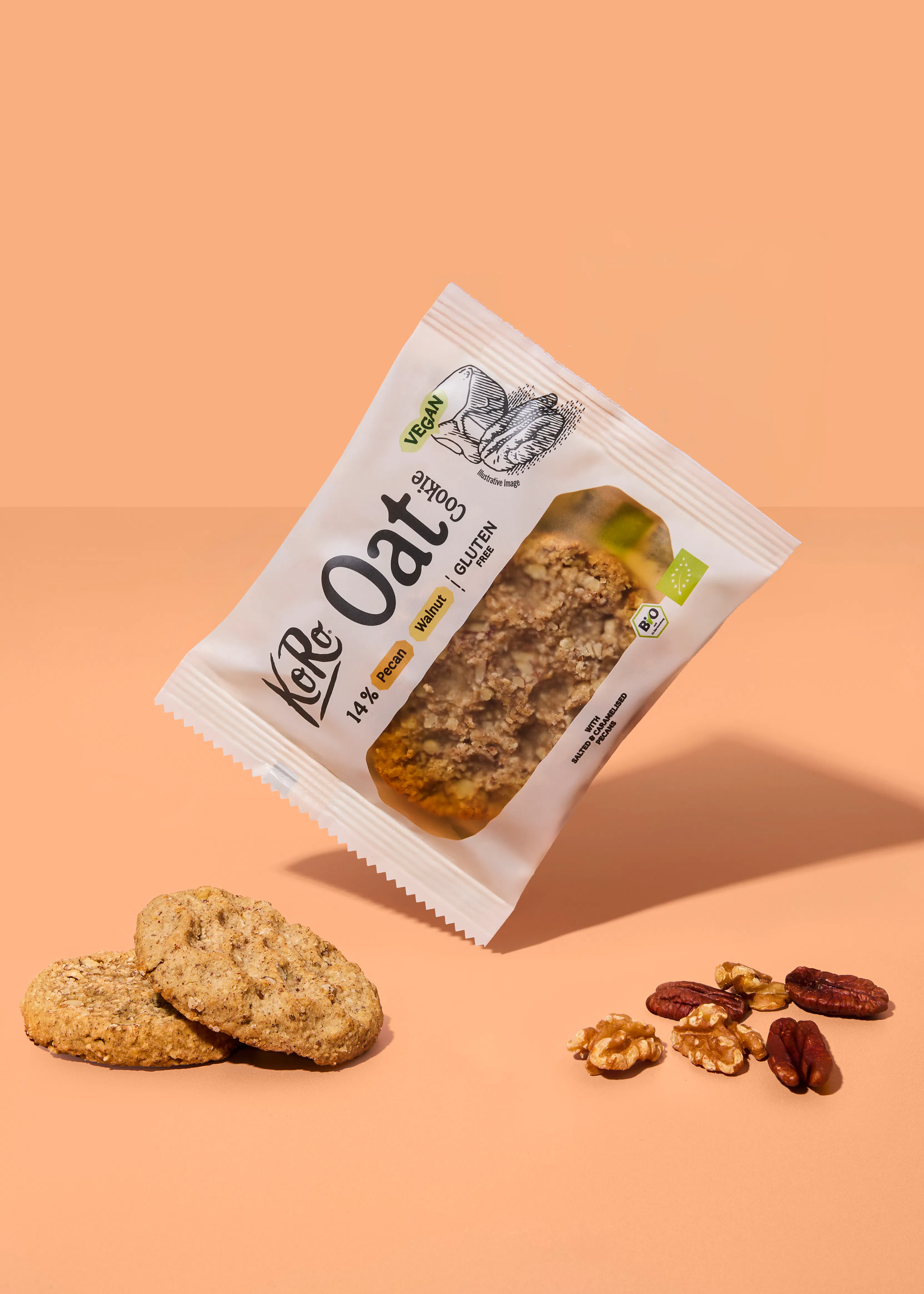 a package of koro vegan oat cookie with pecan and walnut, displayed with two loose cookies and a small pile of nuts on a light brown background.