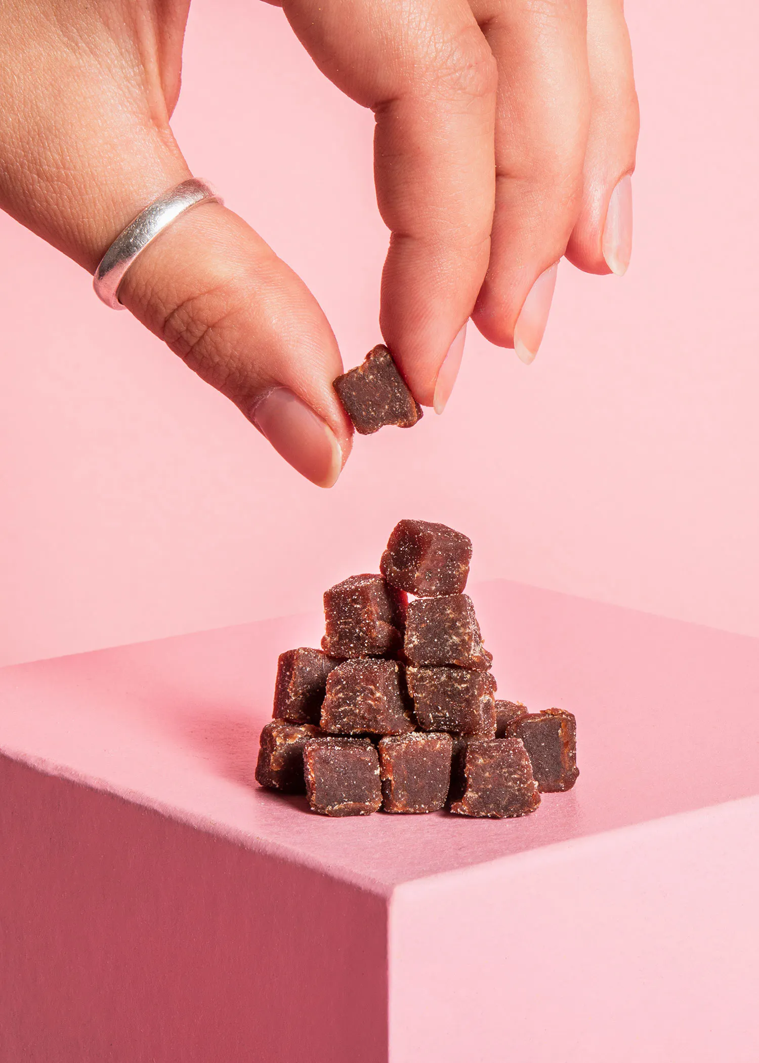 a hand is reaching for a piece of candy on a pink surface